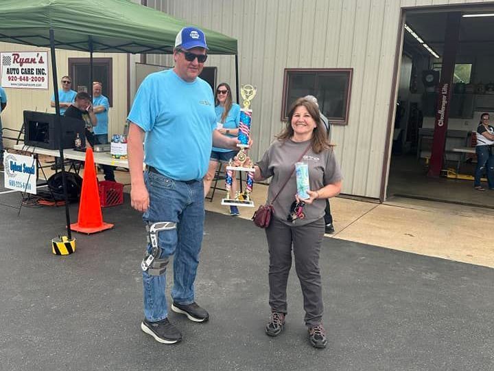 Man with leg brace presents trophy to woman at outdoor event.