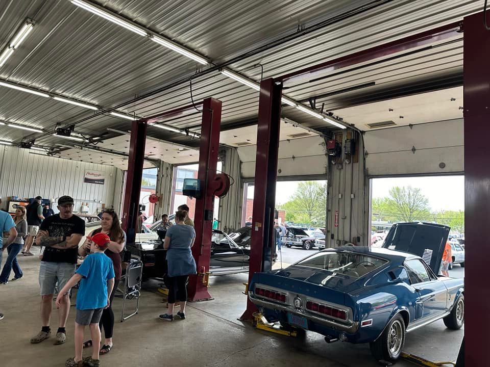 Classic blue car at a car show inside a garage with people viewing and red car lifts.