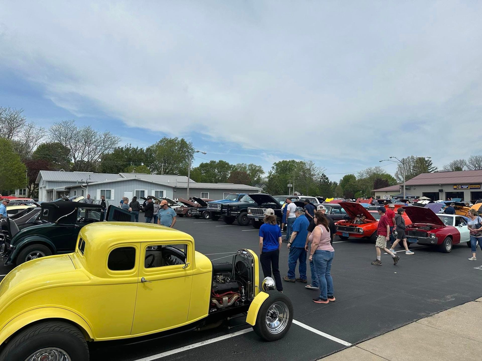 Classic cars on display at an outdoor car show; people viewing and admiring them on a cloudy day.