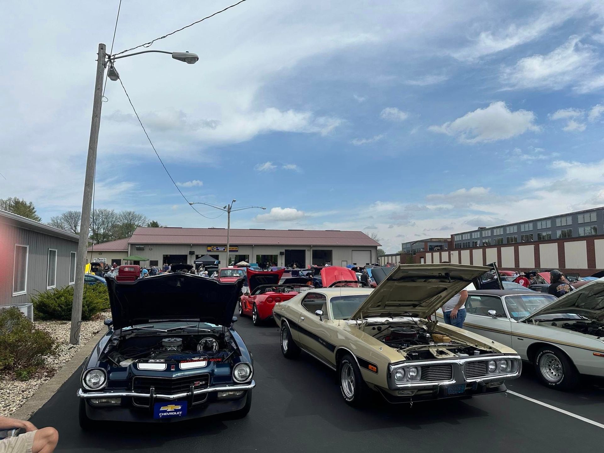 Classic cars on display with open hoods at an outdoor car show under a cloudy sky.