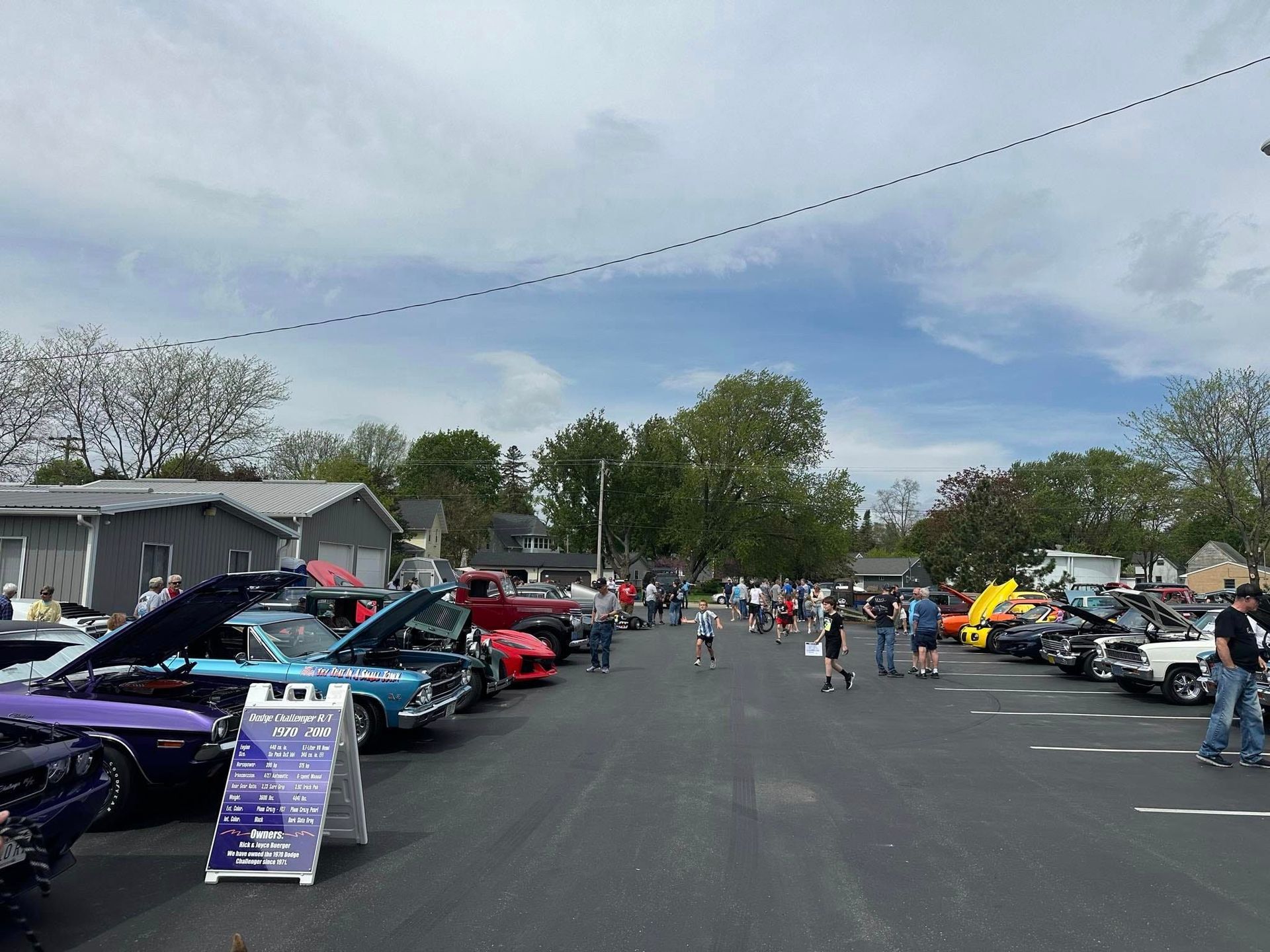 Car show with classic vehicles on display; crowd of people, overcast sky.