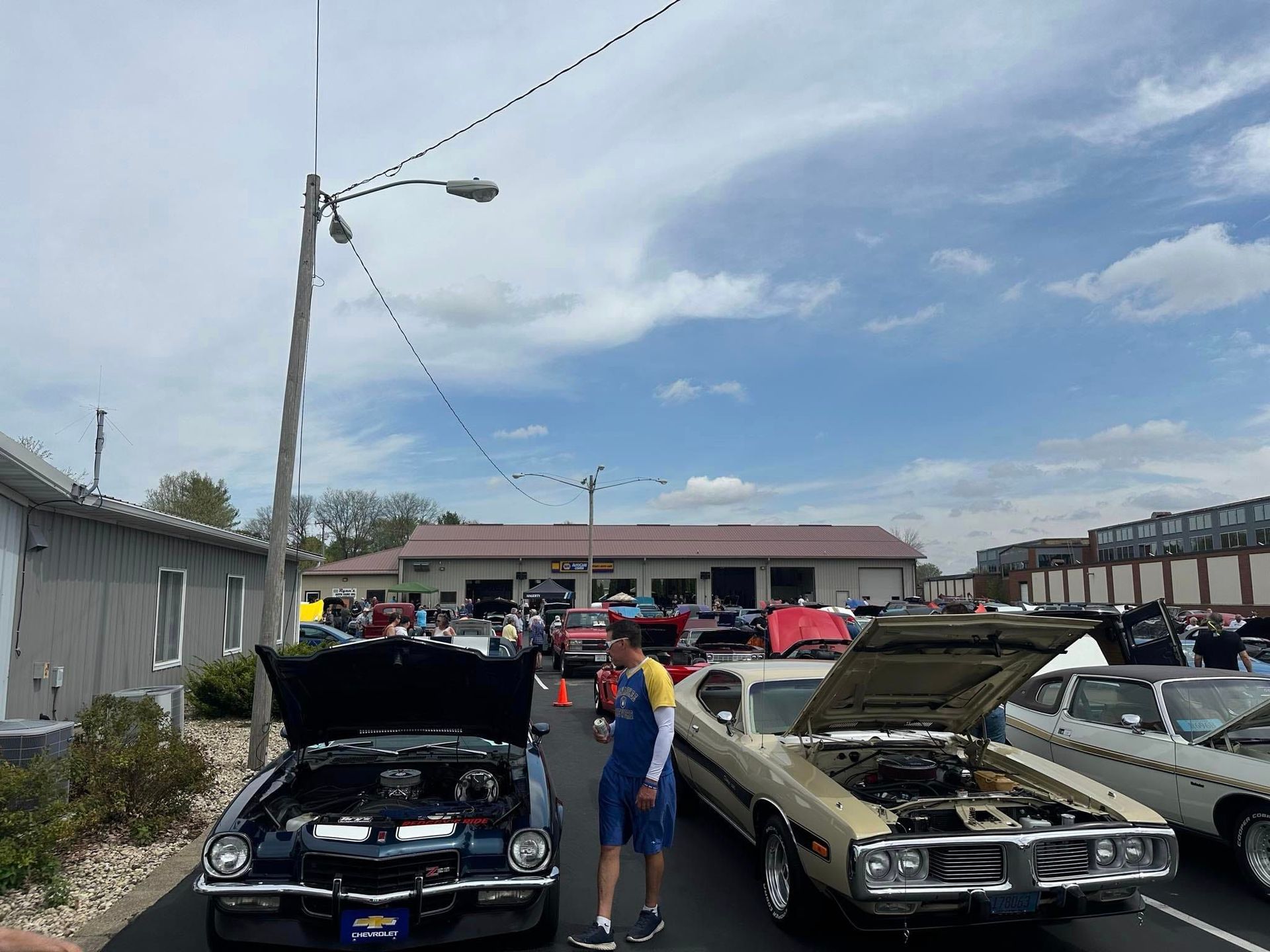 Classic cars on display at an outdoor car show. People are looking at the cars under a cloudy sky.