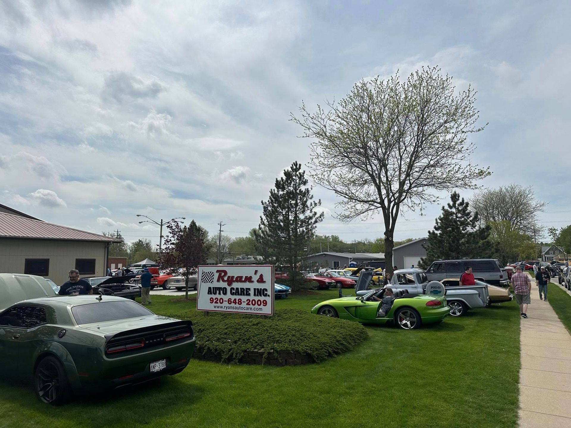 Car show at Ryan's Auto Care Inc., with vintage cars displayed on a grassy lawn under a cloudy sky.