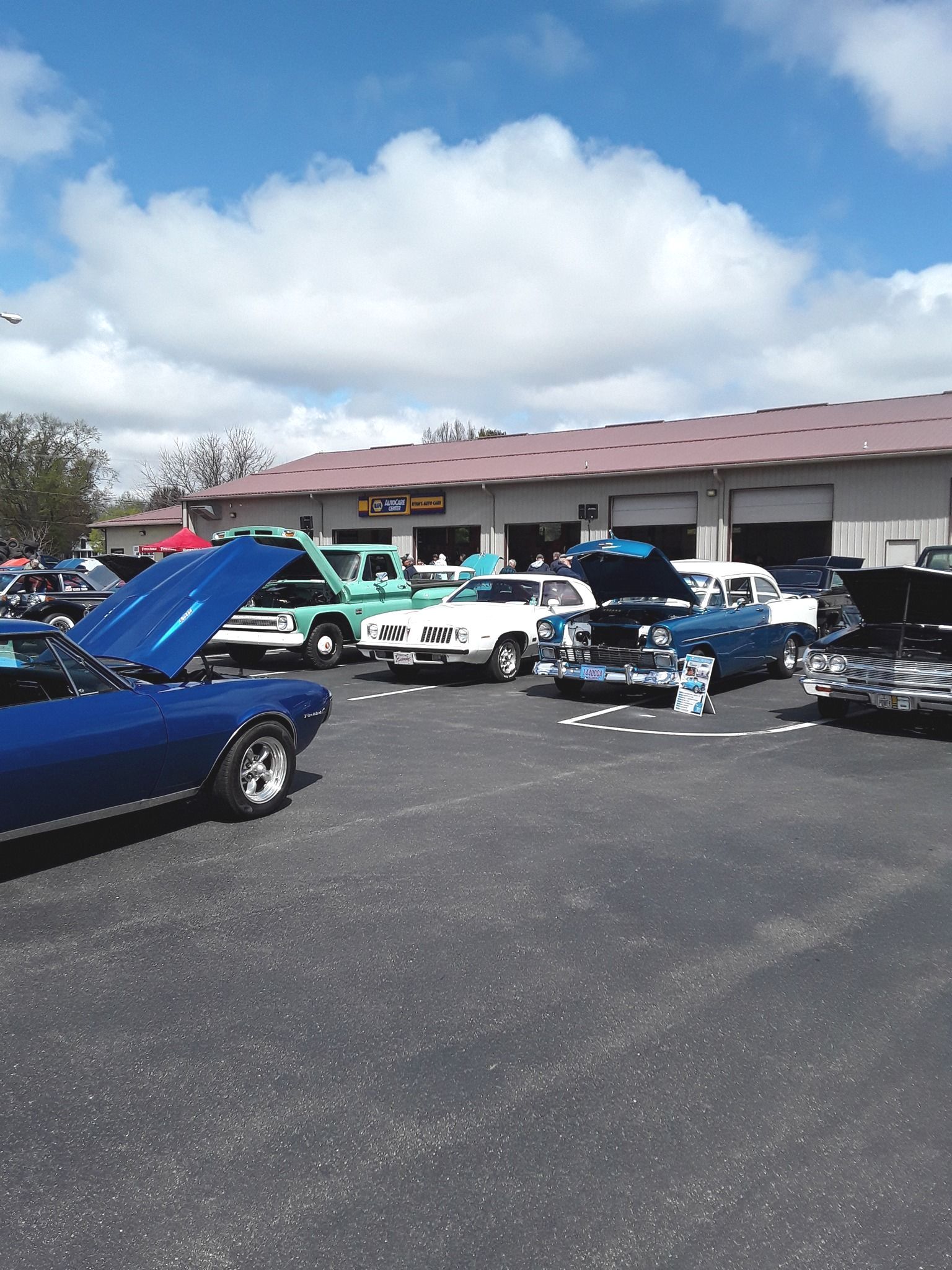 Classic cars on display at an outdoor car show; blue sky and a building in the background.