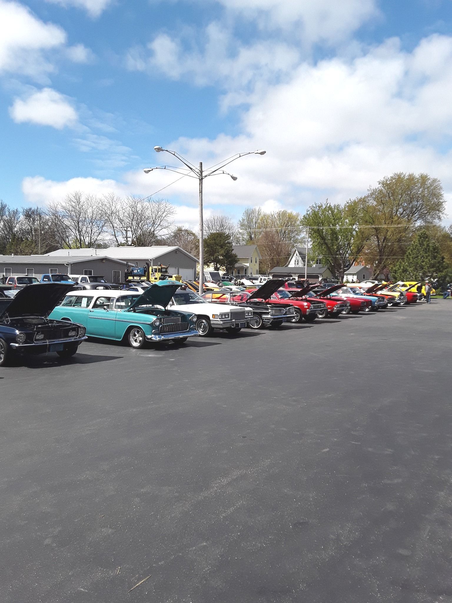Classic cars parked in a lot on a sunny day. Hoods are open, showcasing engines.