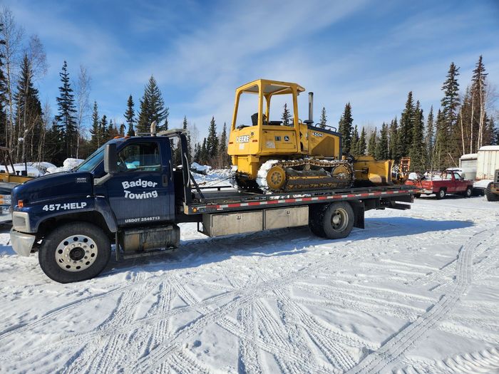 a badger towing truck is carrying a yellow deere bulldozer