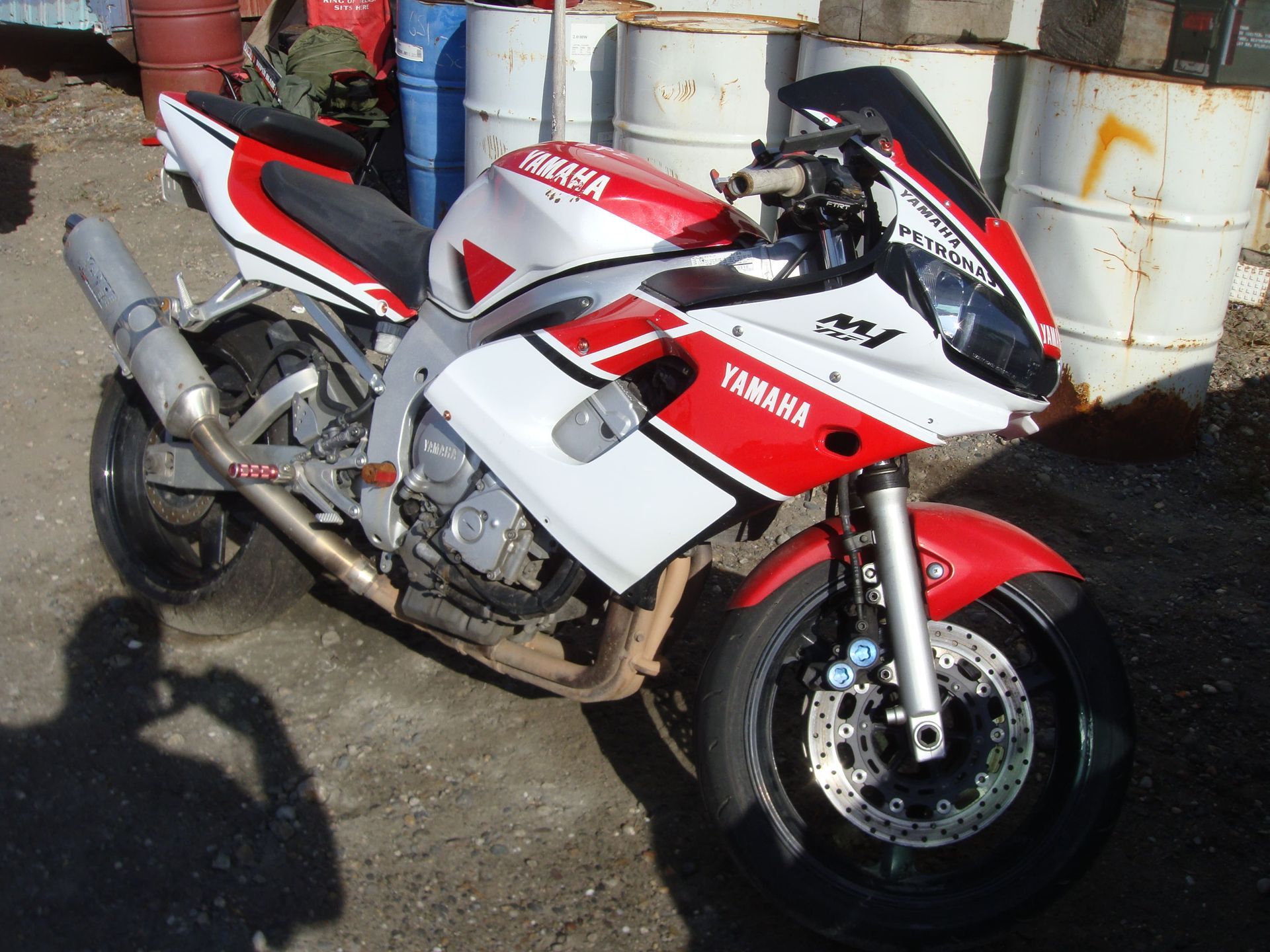 Red and white Yamaha sport motorcycle parked on pavement beside white barrels.