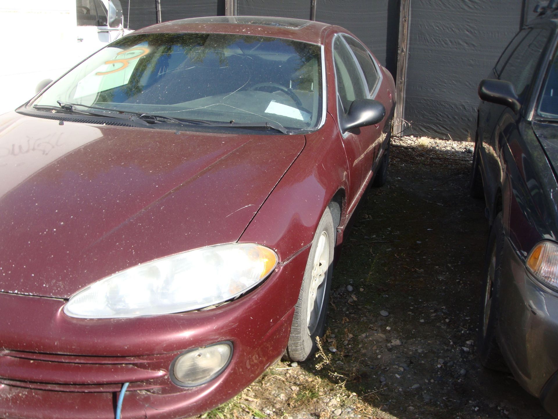 Red car parked tightly beside a dark car in a narrow driveway or parking area.