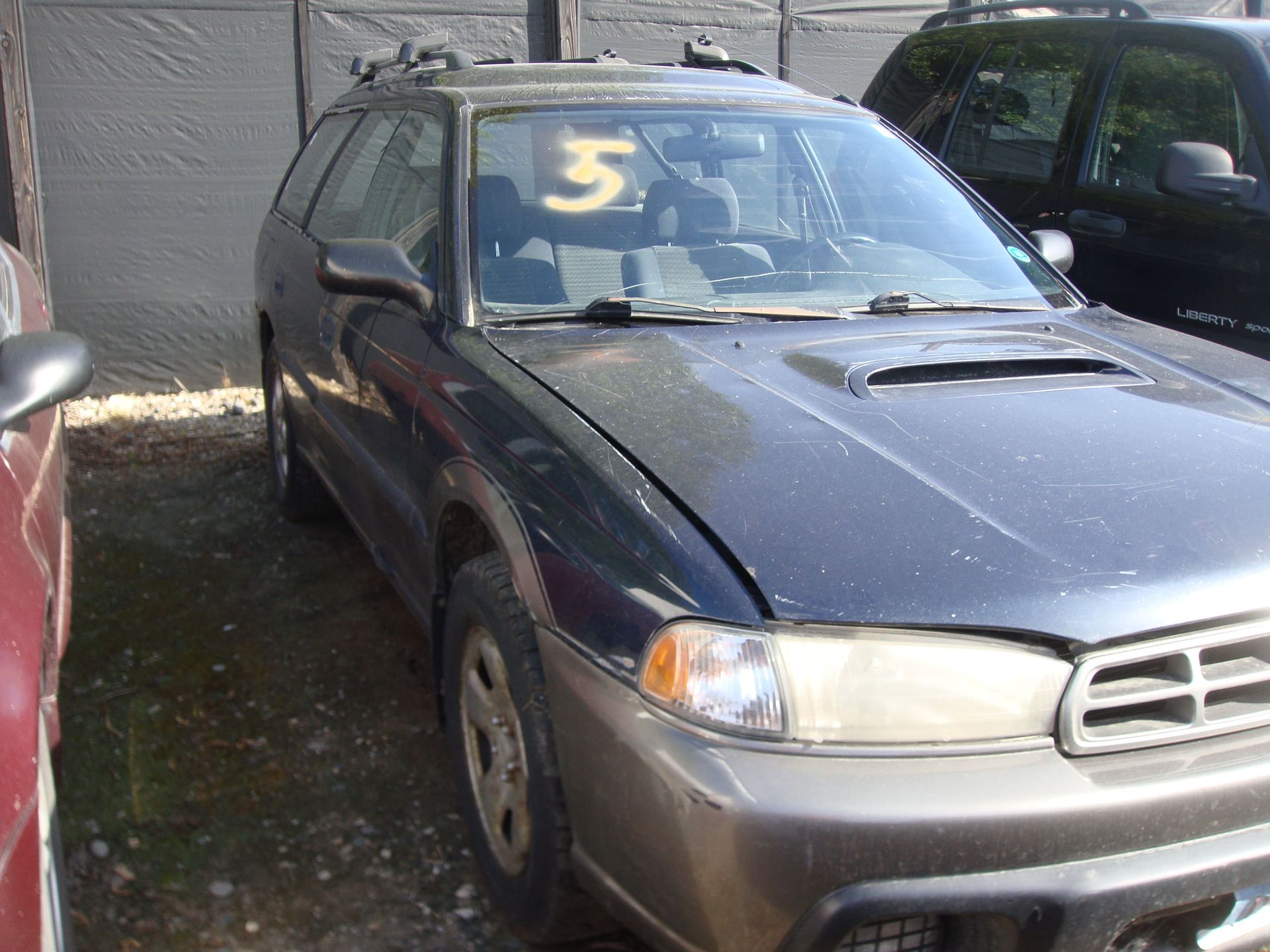 Gray wagon with a yellow number 5 on the windshield, parked beside another car in a lot