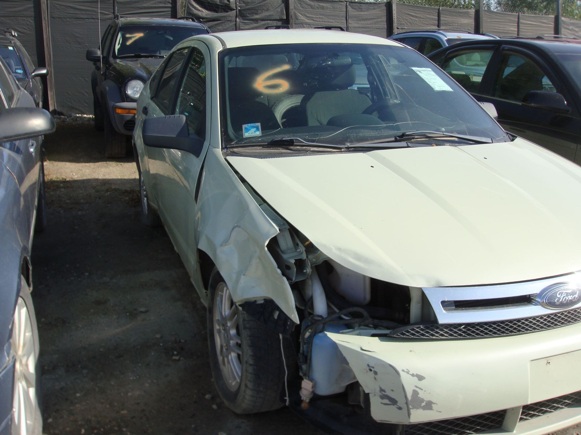 Damaged white sedan parked in a lot, with front-left body damage and crumpled hood