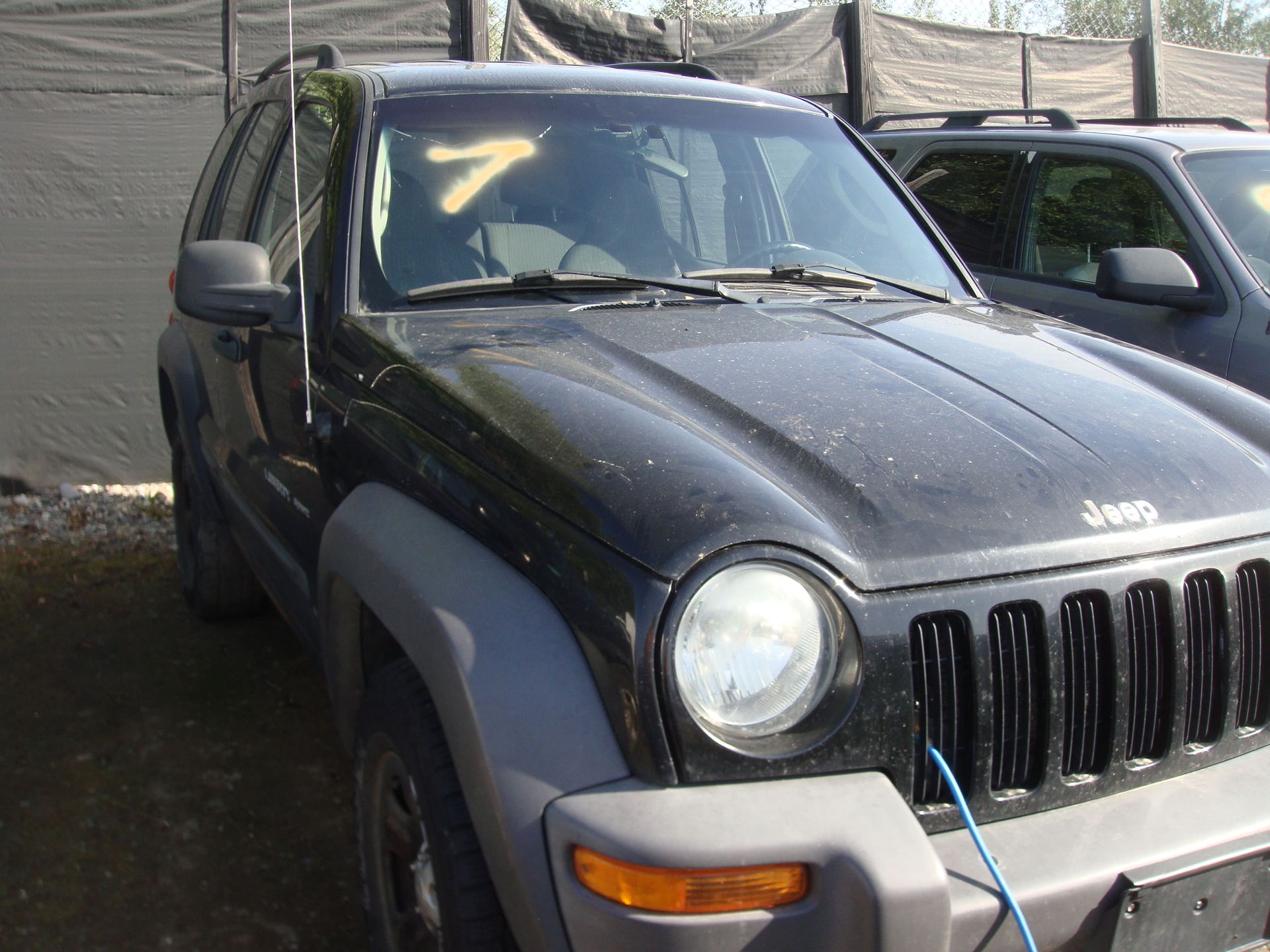 Black Jeep Liberty parked outdoors beside another vehicle, with a blue tow strap on the front.