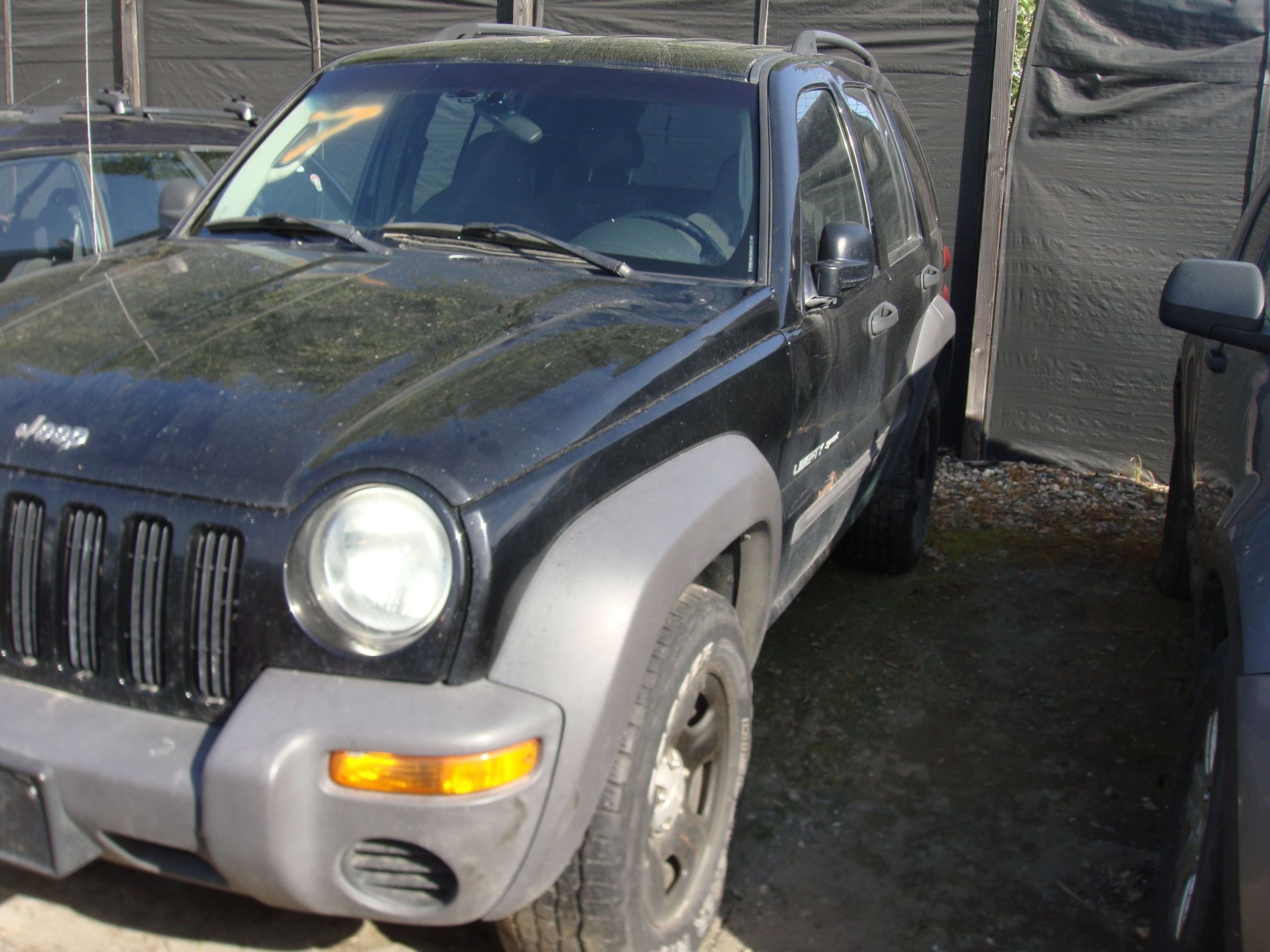 Black Jeep Liberty parked outdoors beside a tarp-covered structure