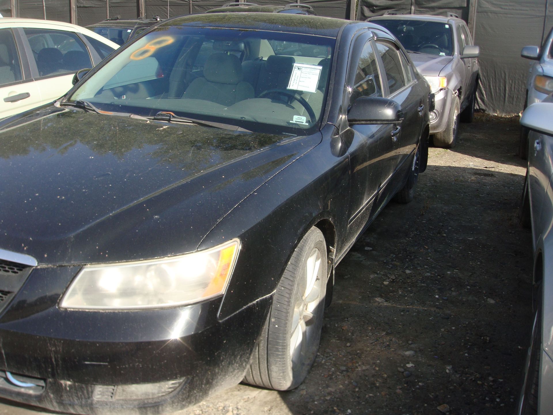Black sedan parked in a tight row of cars, with front-left wheel turned outward.