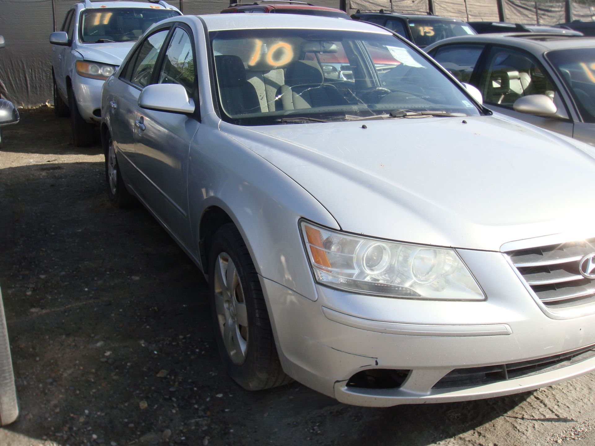 Silver sedan parked in a lot, front-left view with yellow writing on the windshield