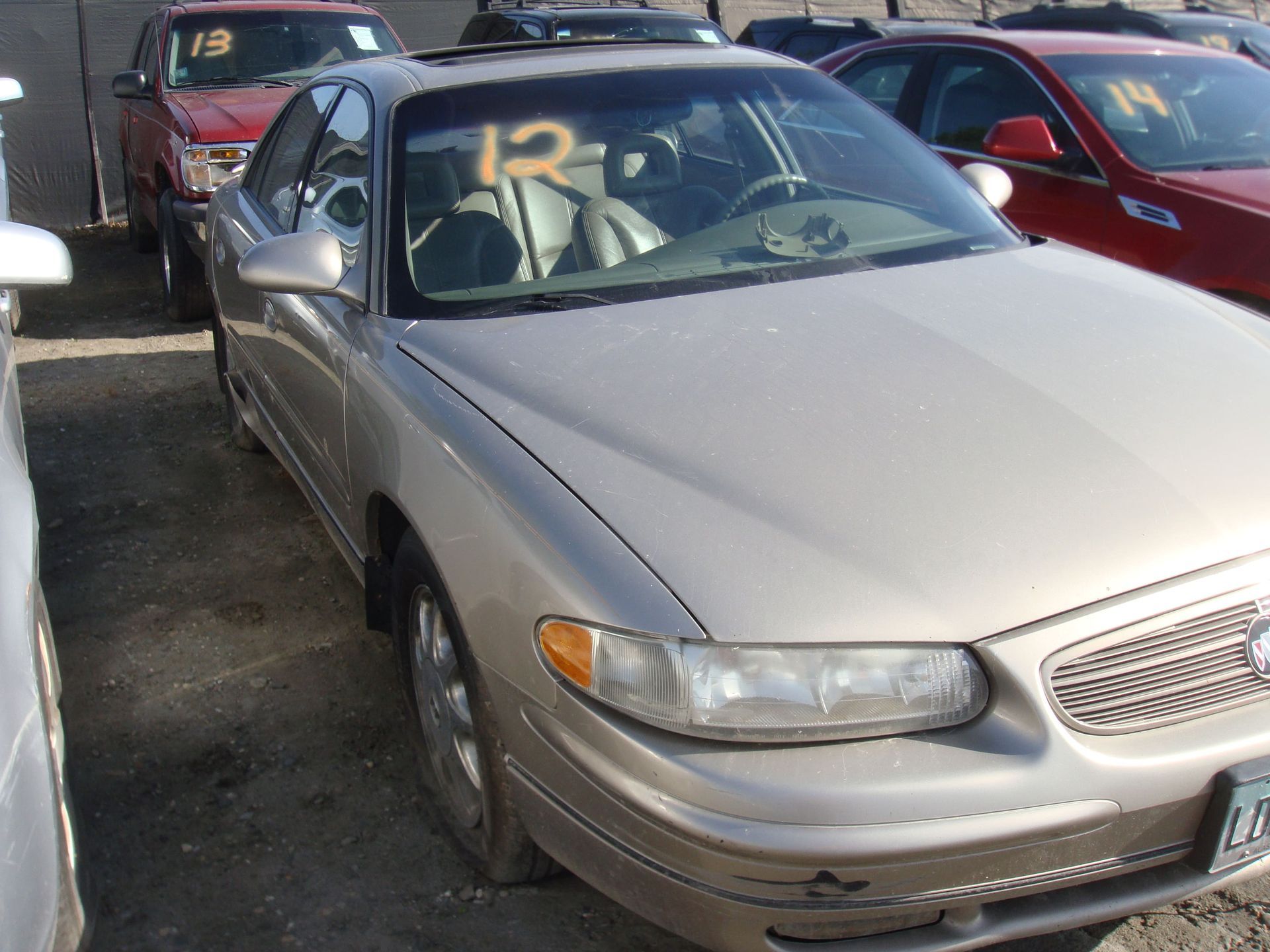 Silver sedan parked in a lot, with other cars nearby and yellow auction numbers on the windshield