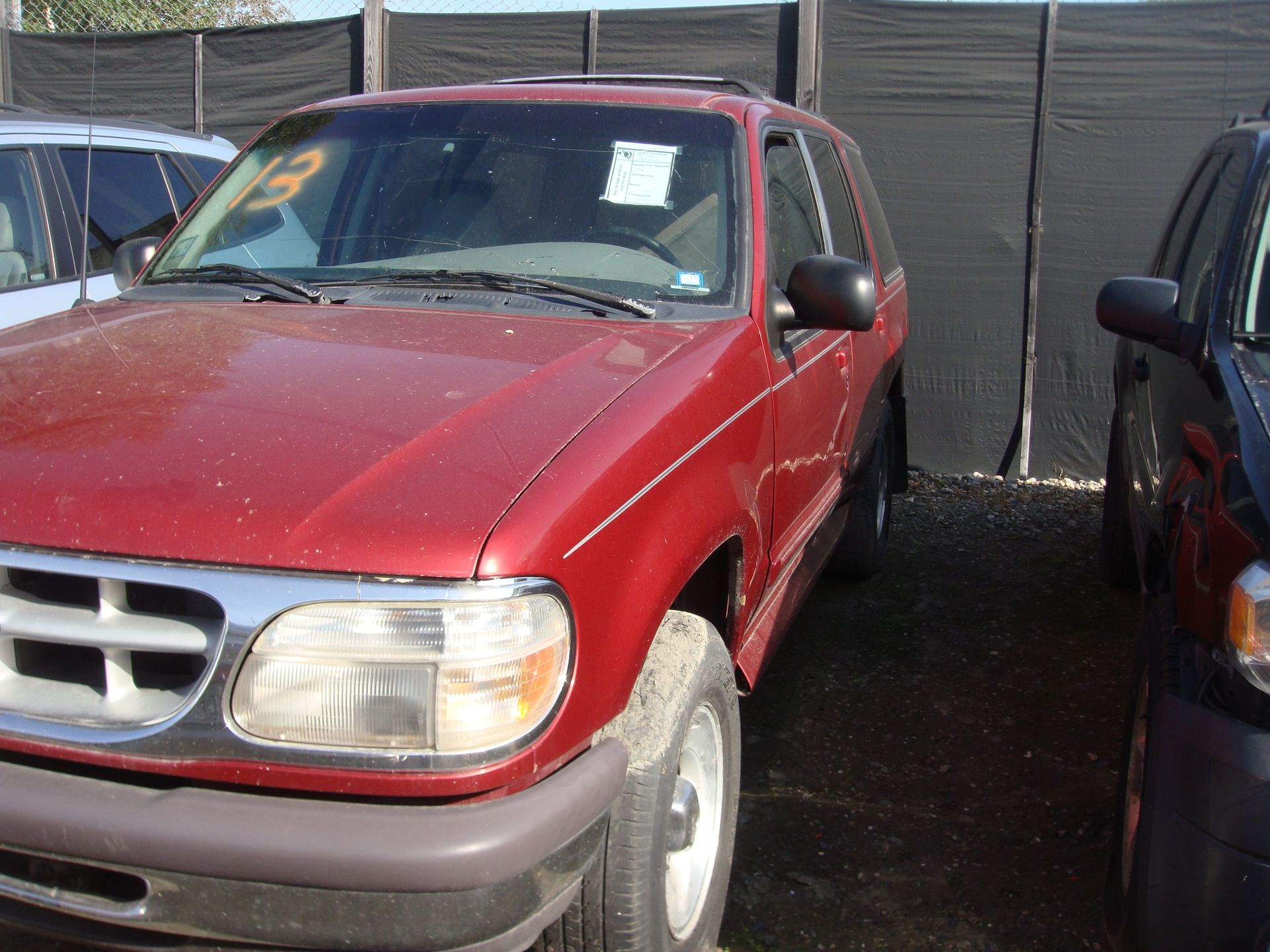 Red SUV parked closely beside another car behind a dark fence.