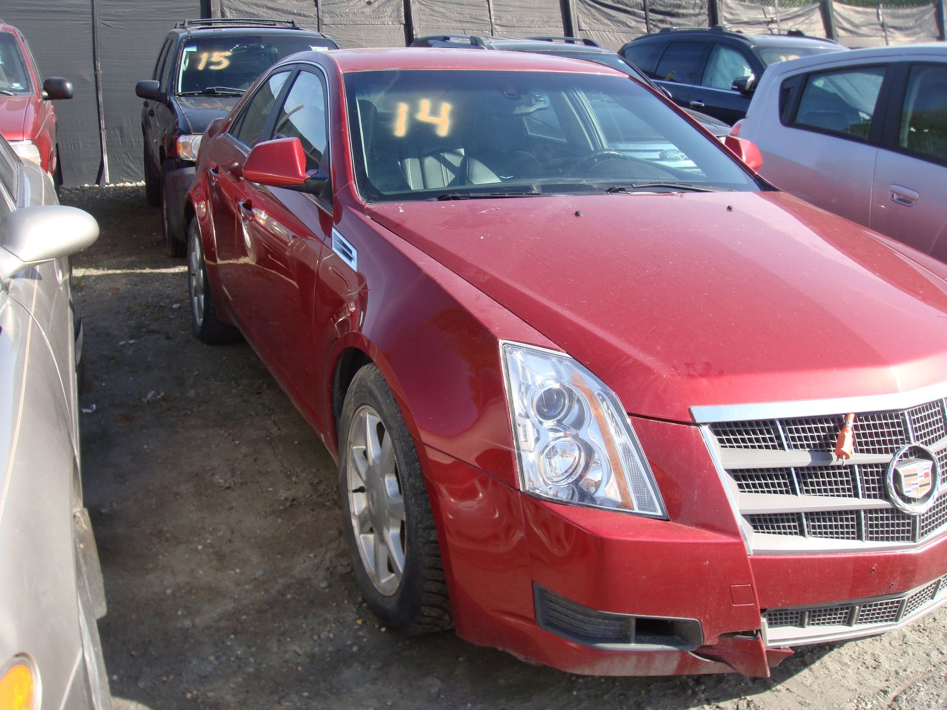 Red Cadillac sedan parked in a lot, with a yellow “14” on the windshield.