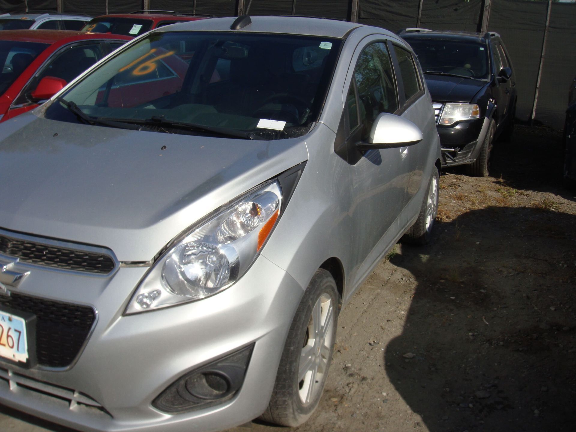 Silver compact car parked in a lot, front-left view, with other vehicles behind it