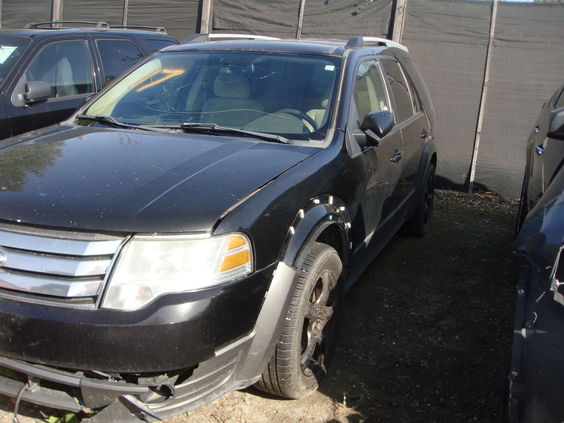 Black SUV parked on a wet lot beside a building and fence
