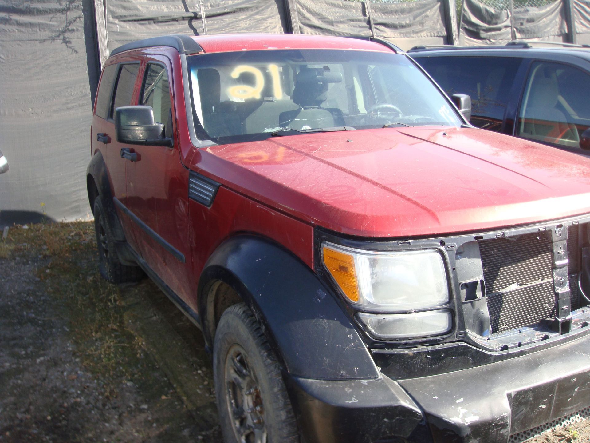 Red pickup truck with a damaged front end and yellow markings on the windshield, parked beside another vehicle.