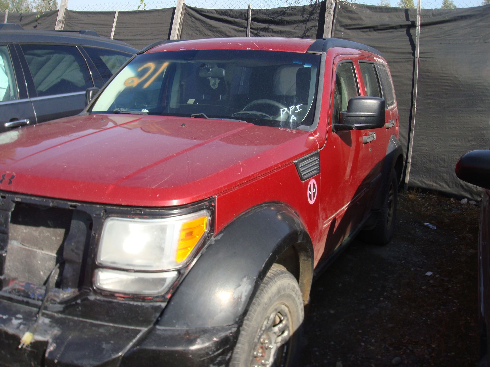 Red pickup truck parked outdoors beside a fence, with a black front bumper and muddy tires.