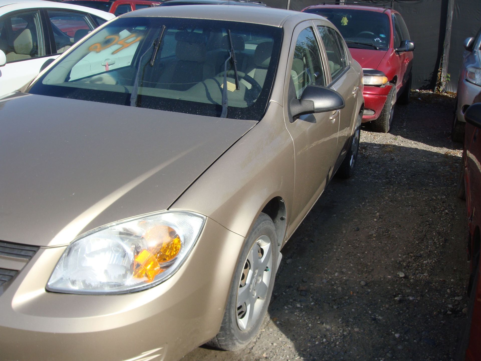 Beige sedan parked in a lot, with a red car behind it and another car beside it.