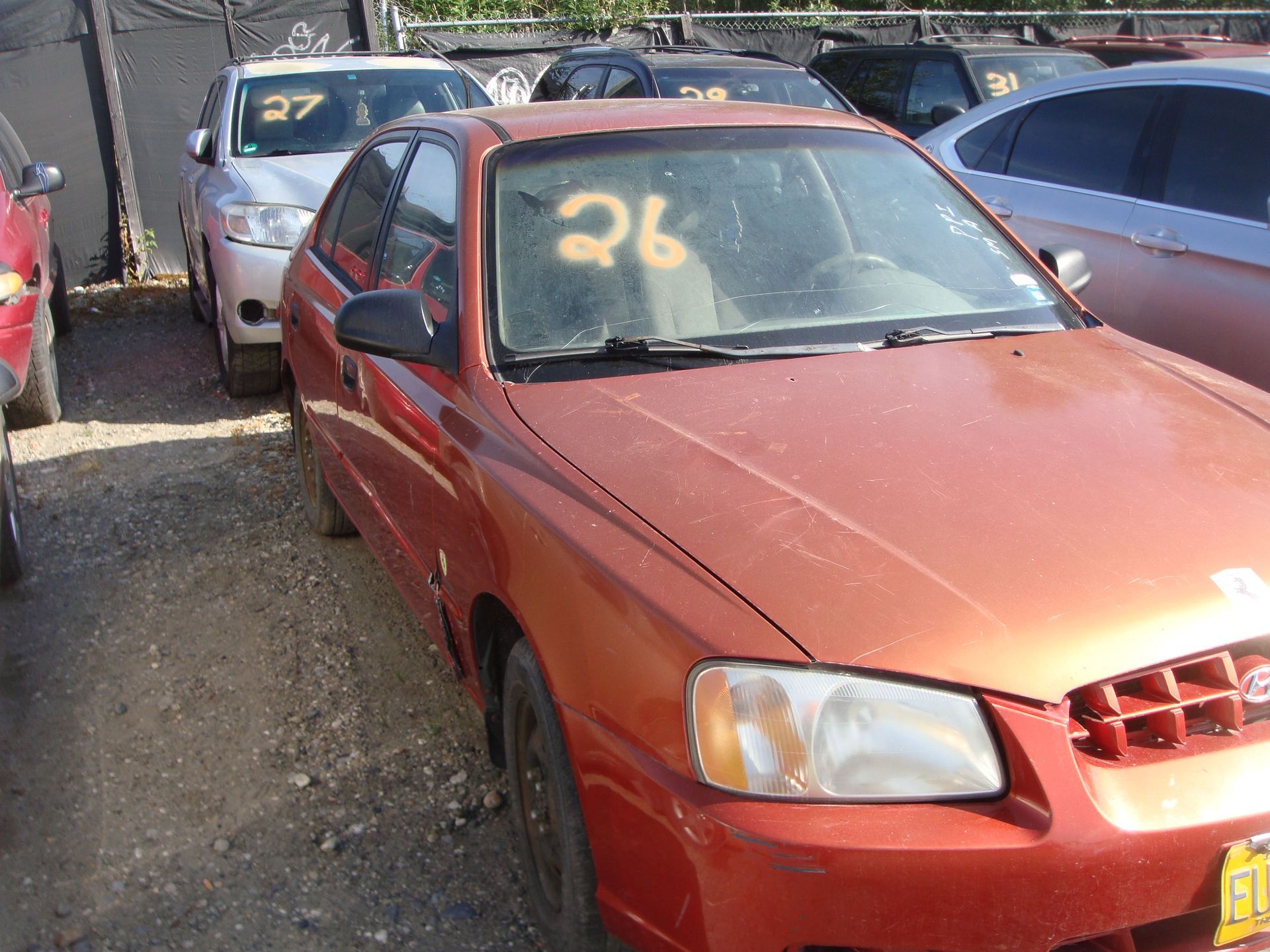 Red sedan parked in a crowded lot, with the number 26 marked on the windshield.