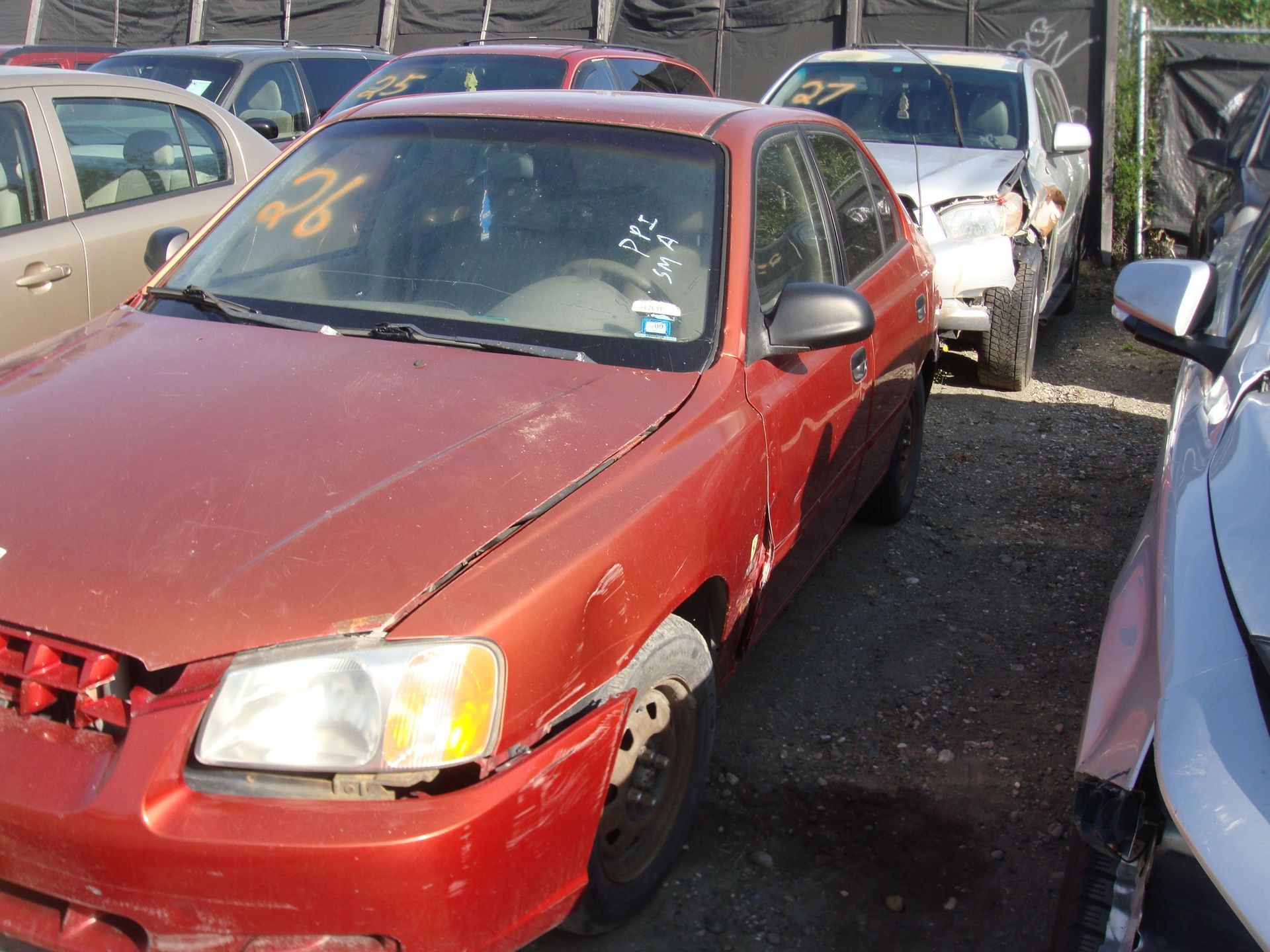 Red sedan with damaged front end parked in a crowded junkyard lot