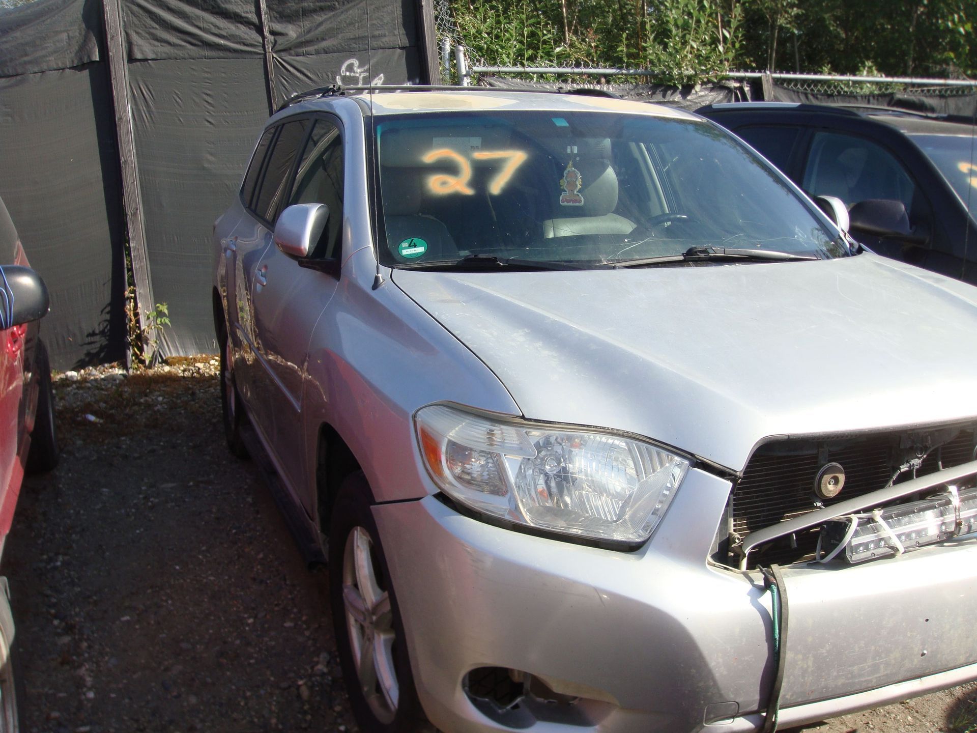 Silver car with front-end damage and a large orange “27” on the windshield, parked outdoors