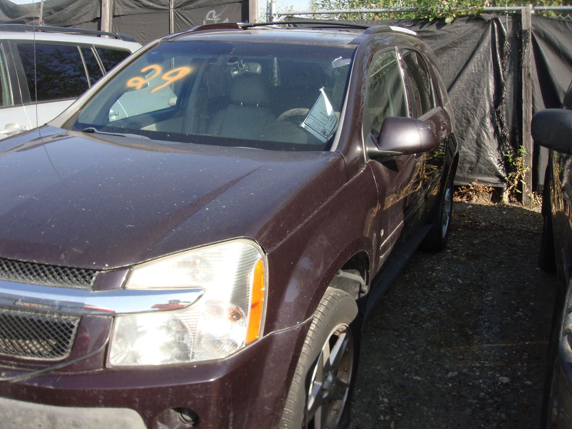 Maroon SUV parked beside a tarp-covered fence in a lot