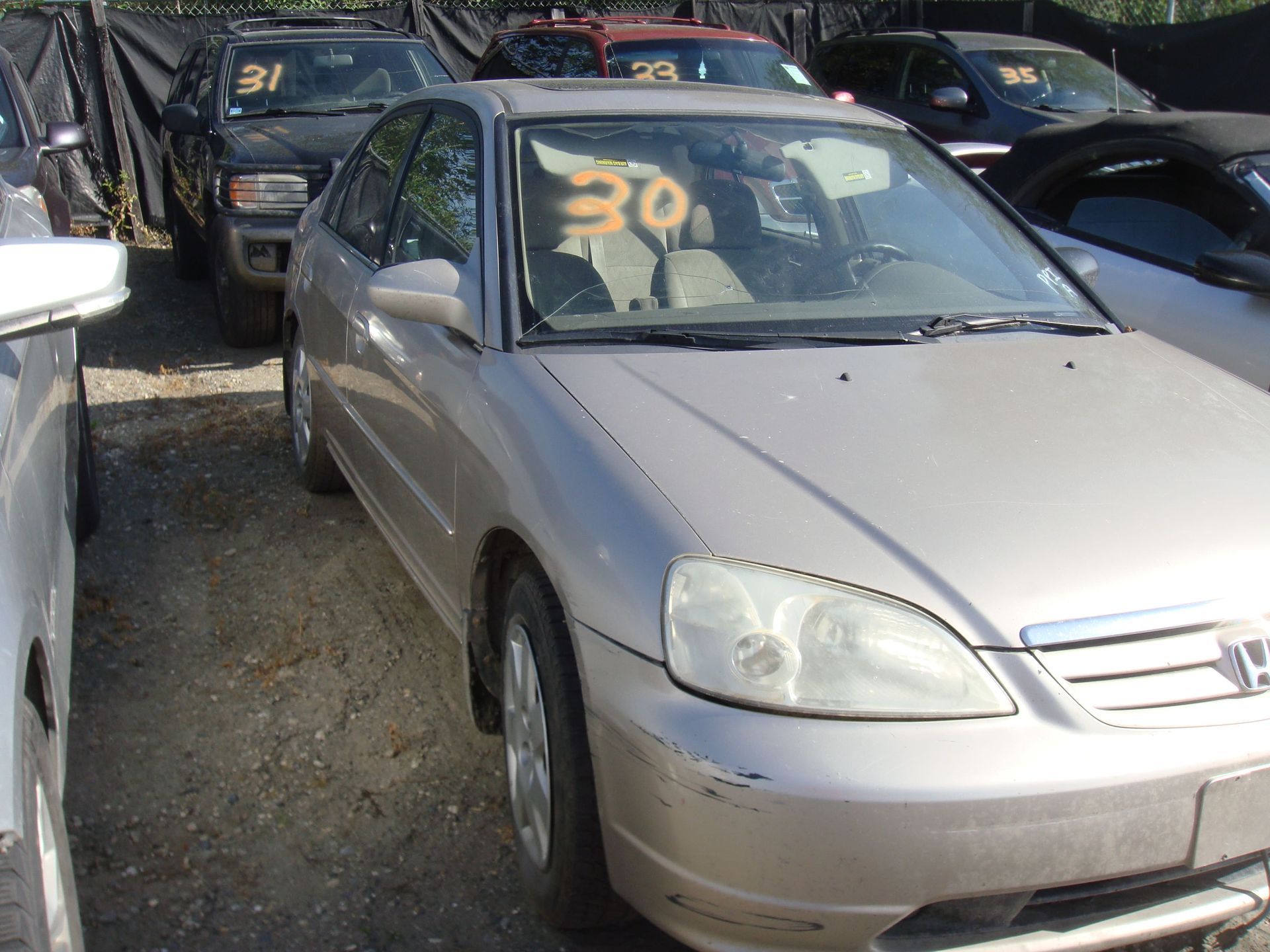 Silver sedan in a crowded used car lot, with orange “30” and black “31” signs on the windshields.