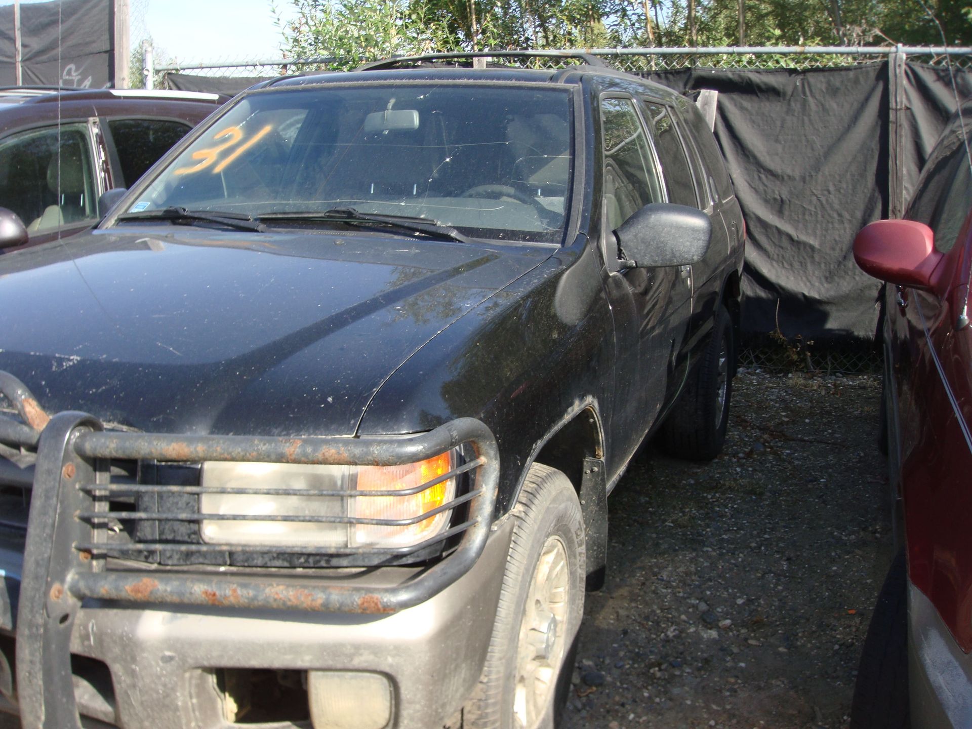 Dusty black pickup truck parked between cars in a gravel lot, front-left view.