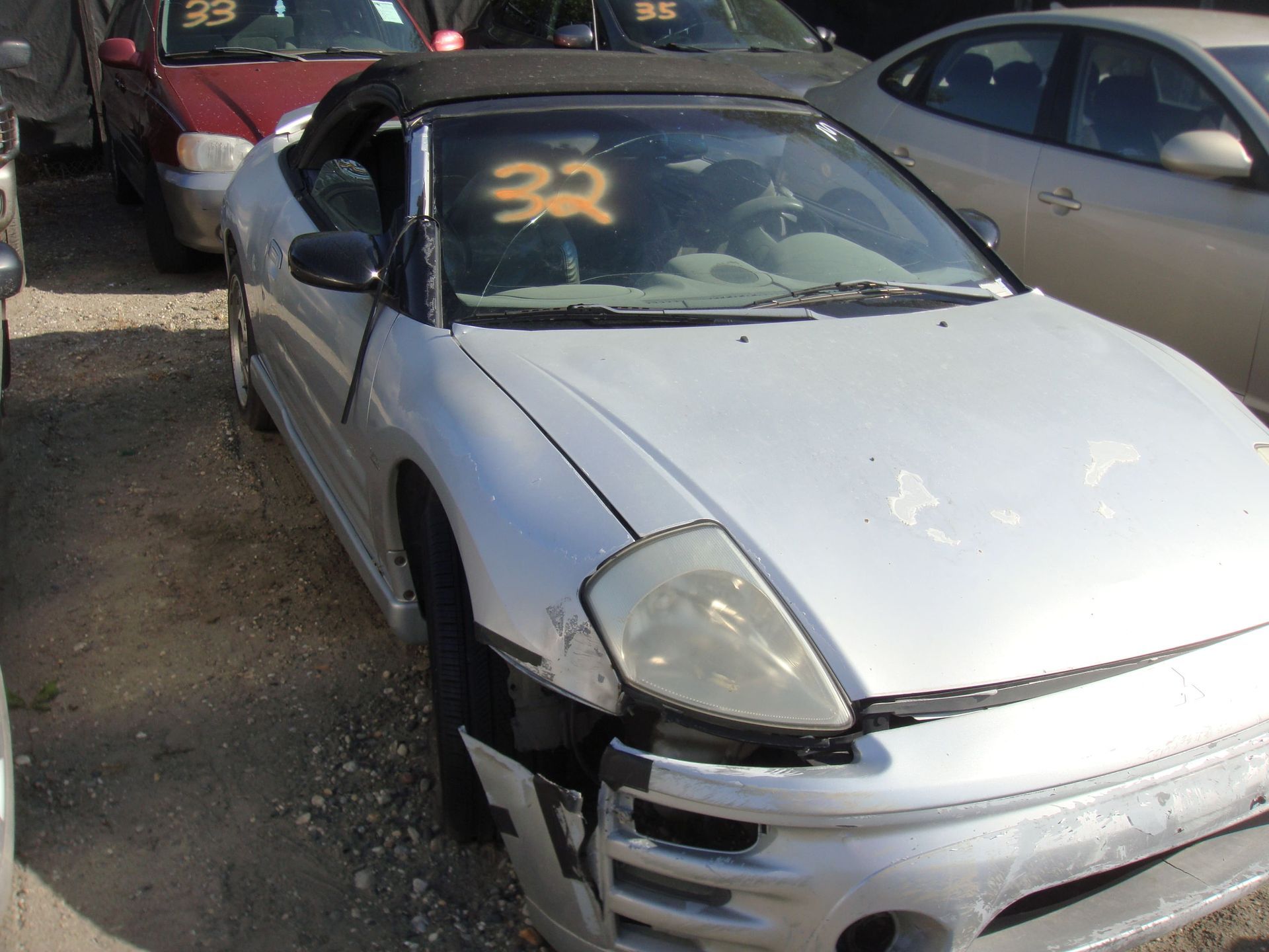 Silver damaged sports car with front-end damage in a junkyard, marked “32” on the windshield