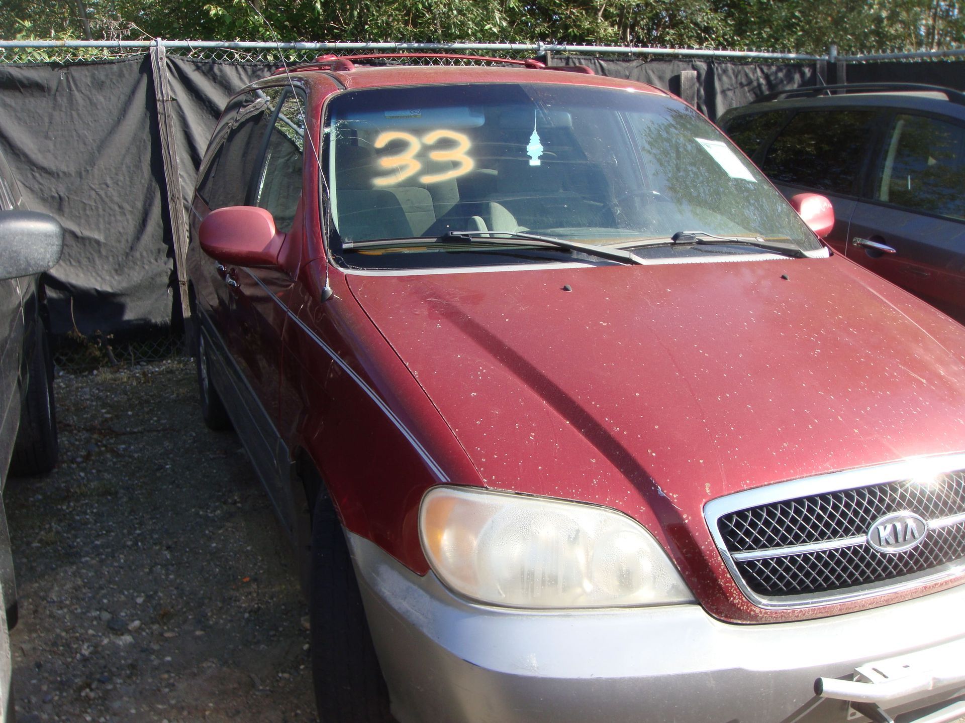 Maroon Kia sedan parked outdoors with a large yellow “33” on the windshield