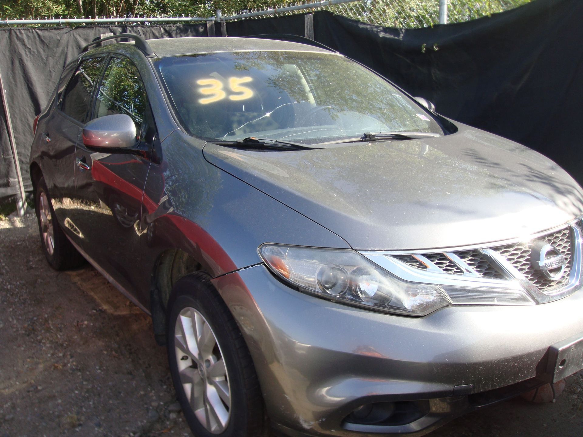 Silver SUV with yellow number 35 on windshield, parked outdoors by a black fence