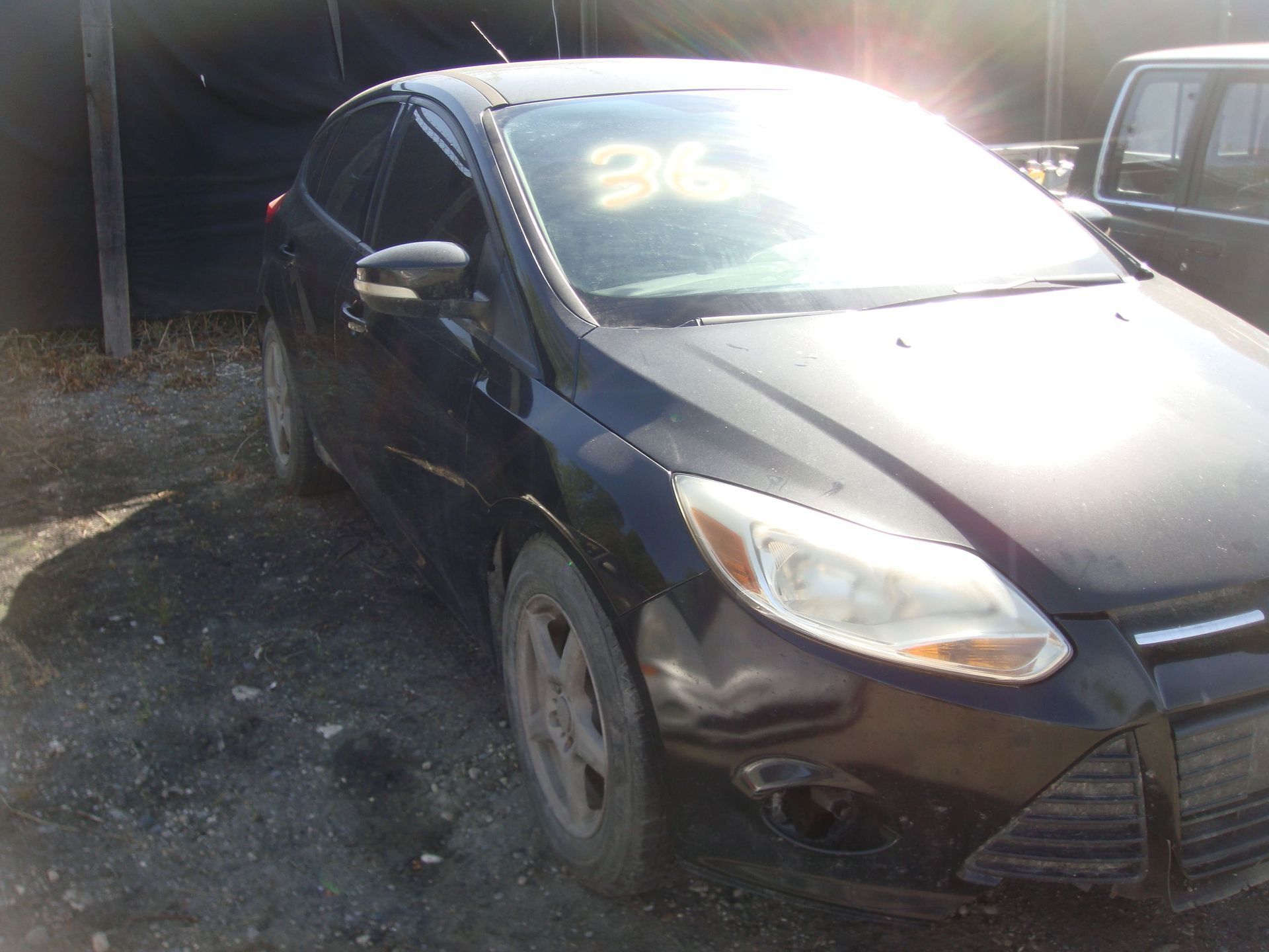 Black sedan parked outdoors in bright sunlight, front-left view with dusty wheels.