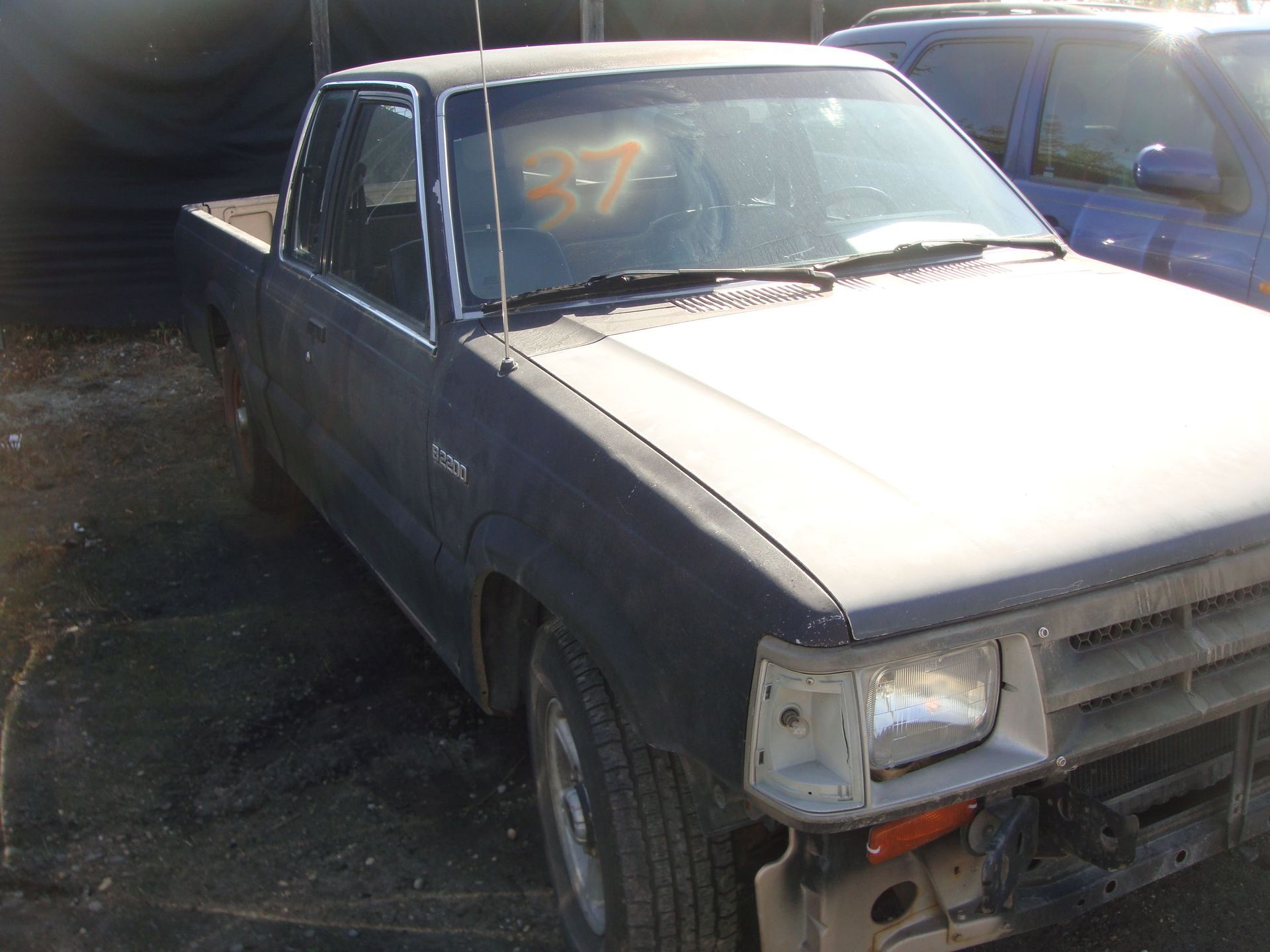 Old gray pickup truck parked outdoors, front damaged and partially missing bumper.