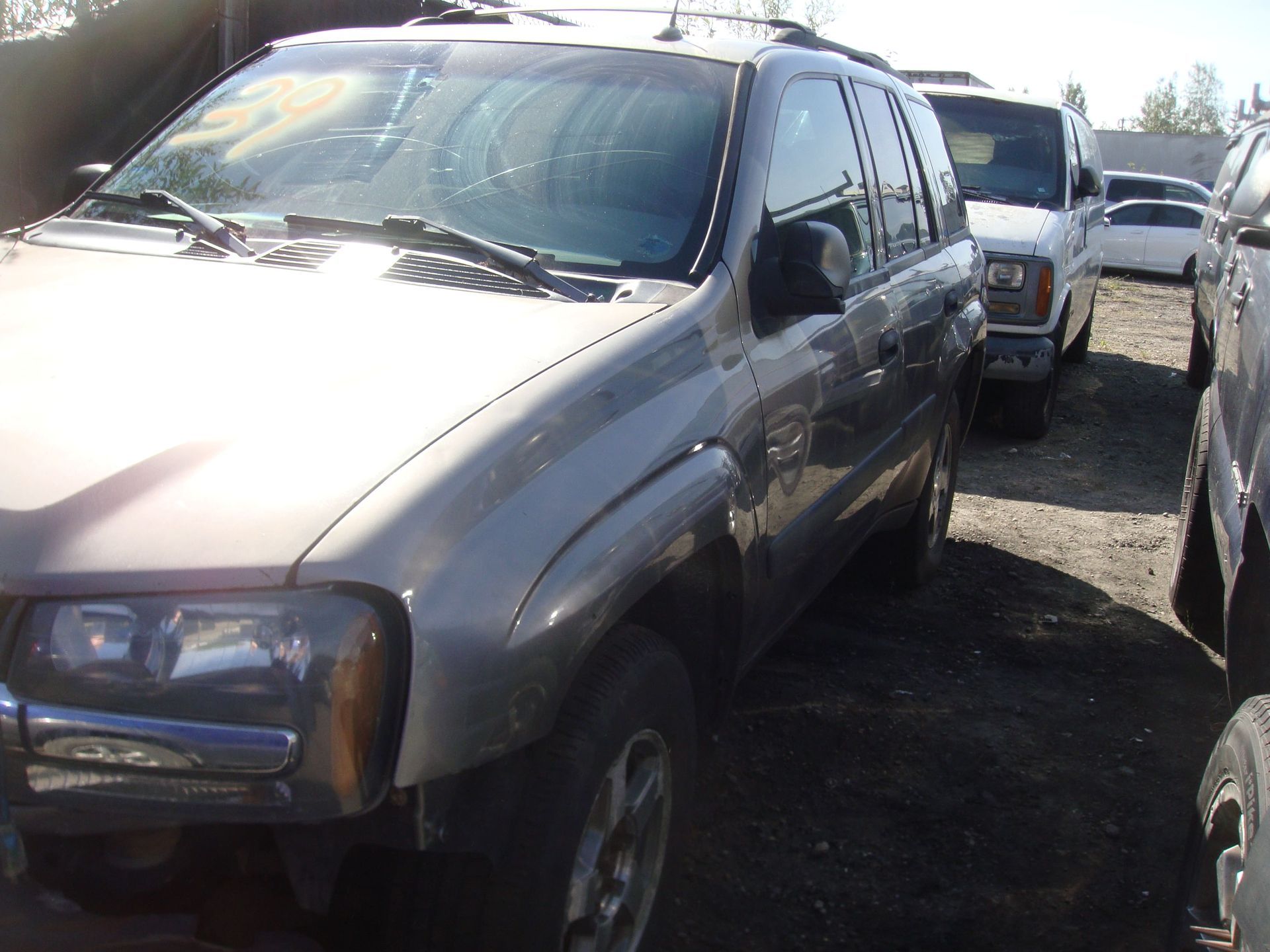Dusty silver SUV parked in a lot beside other vehicles, with front damage visible