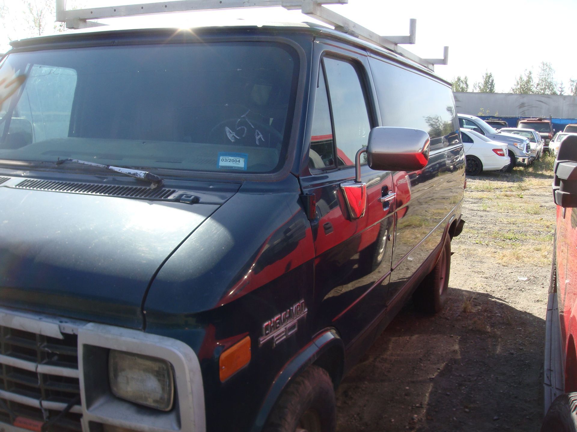 Dark blue van parked outdoors in a gravel lot with other vehicles in the background