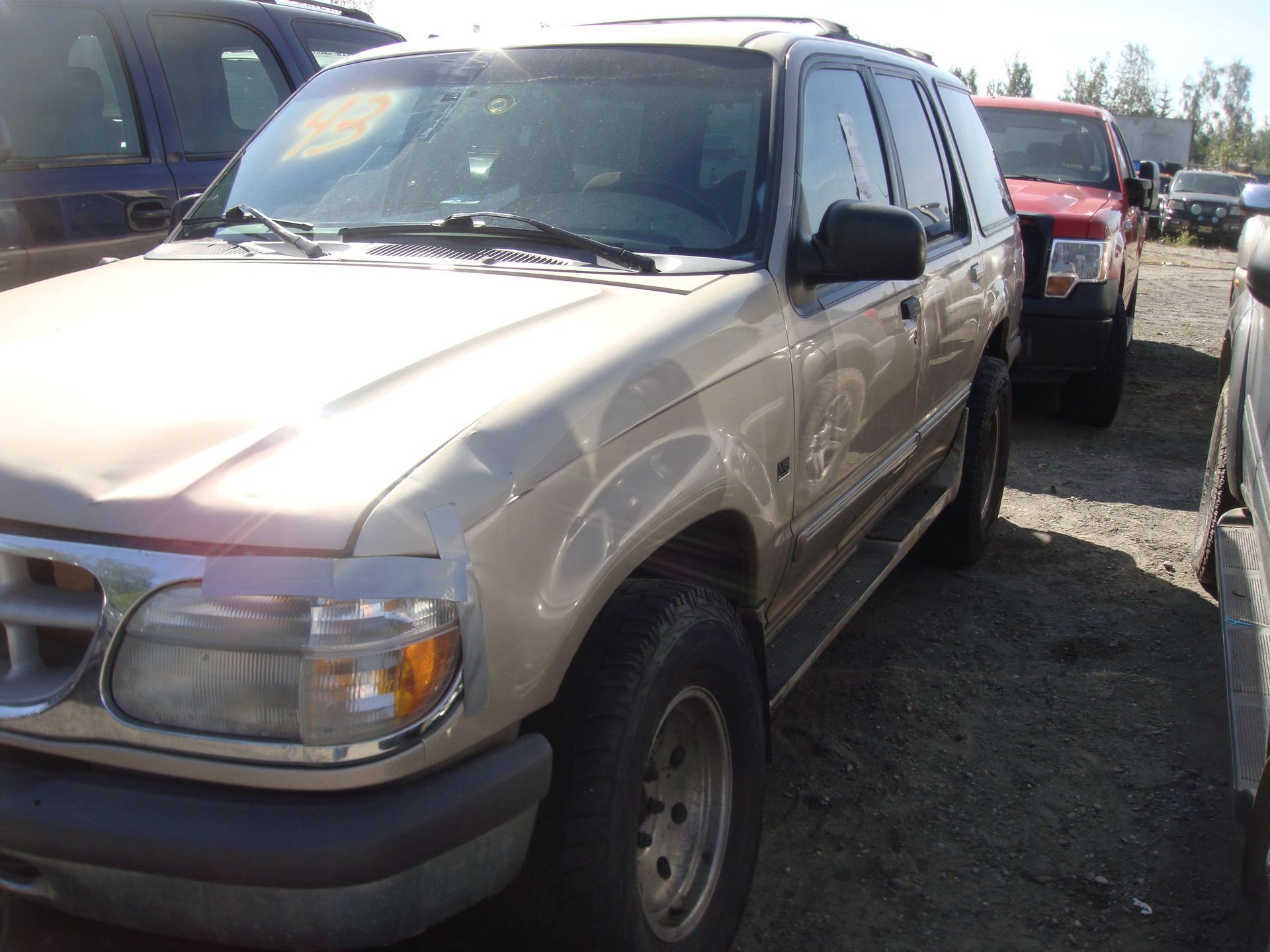 Beige SUV parked in a lot beside other vehicles, front-left view.