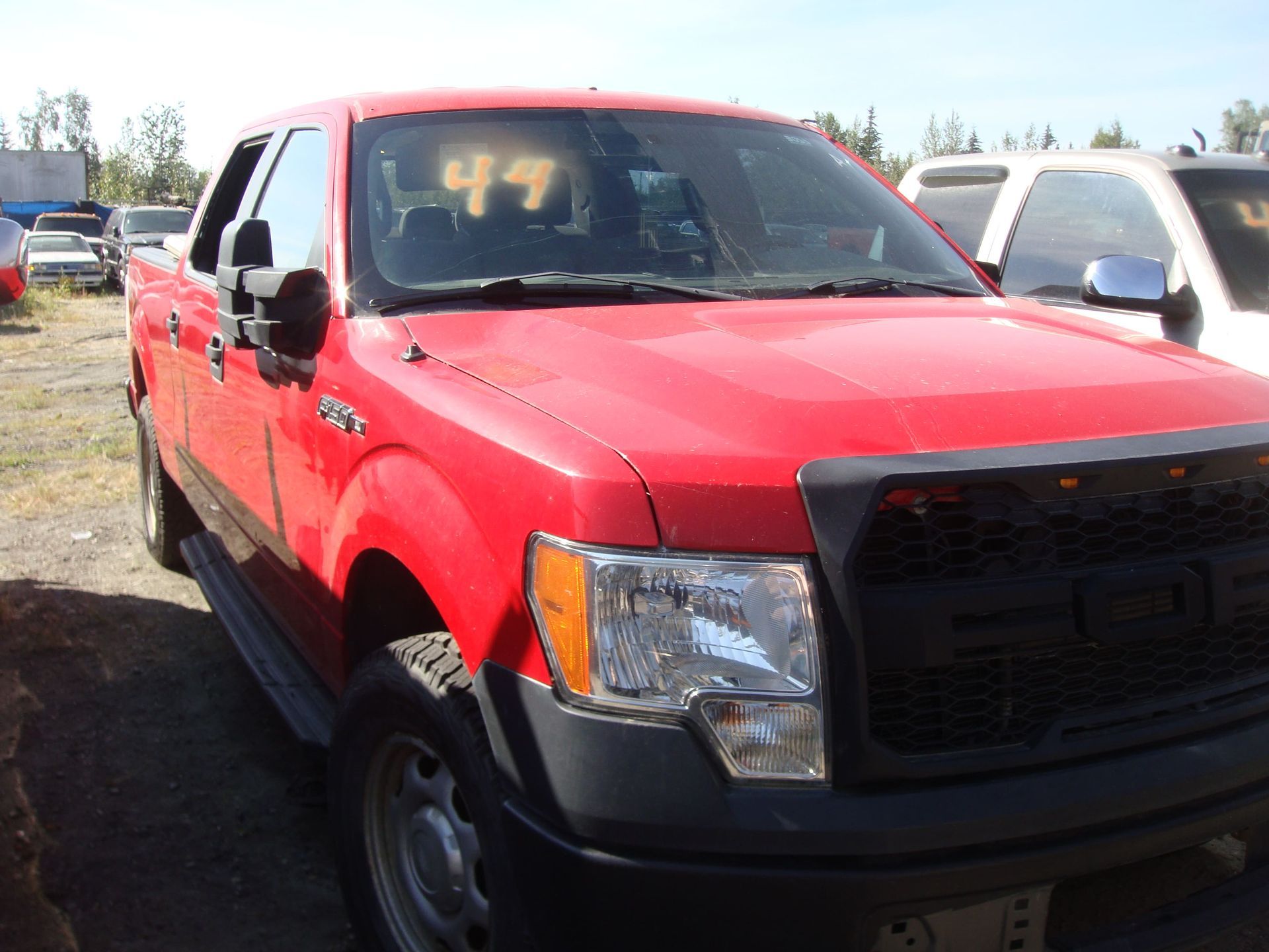 Red pickup truck parked in a lot, with a black grille and silver side mirror.