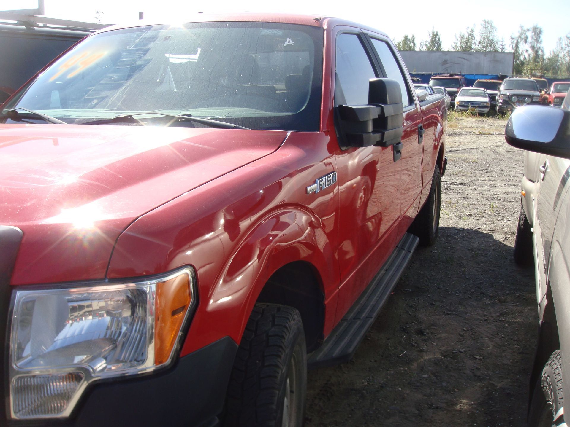 Red pickup truck parked outdoors in a gravel lot, viewed from the front-left side.