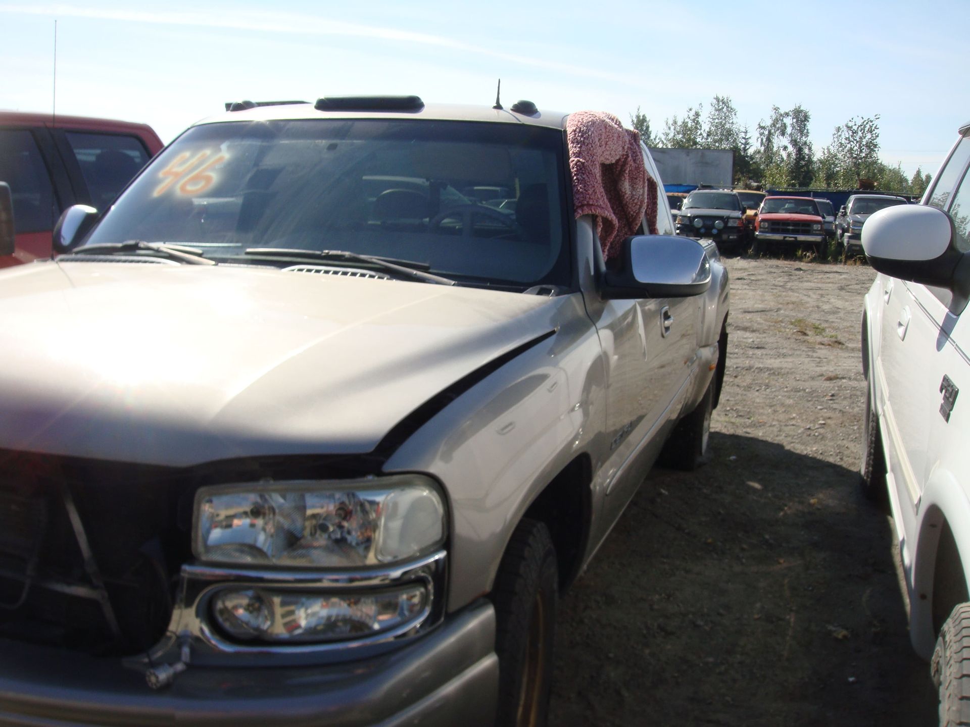 Beige pickup truck in a dusty outdoor lot, parked between other vehicles.
