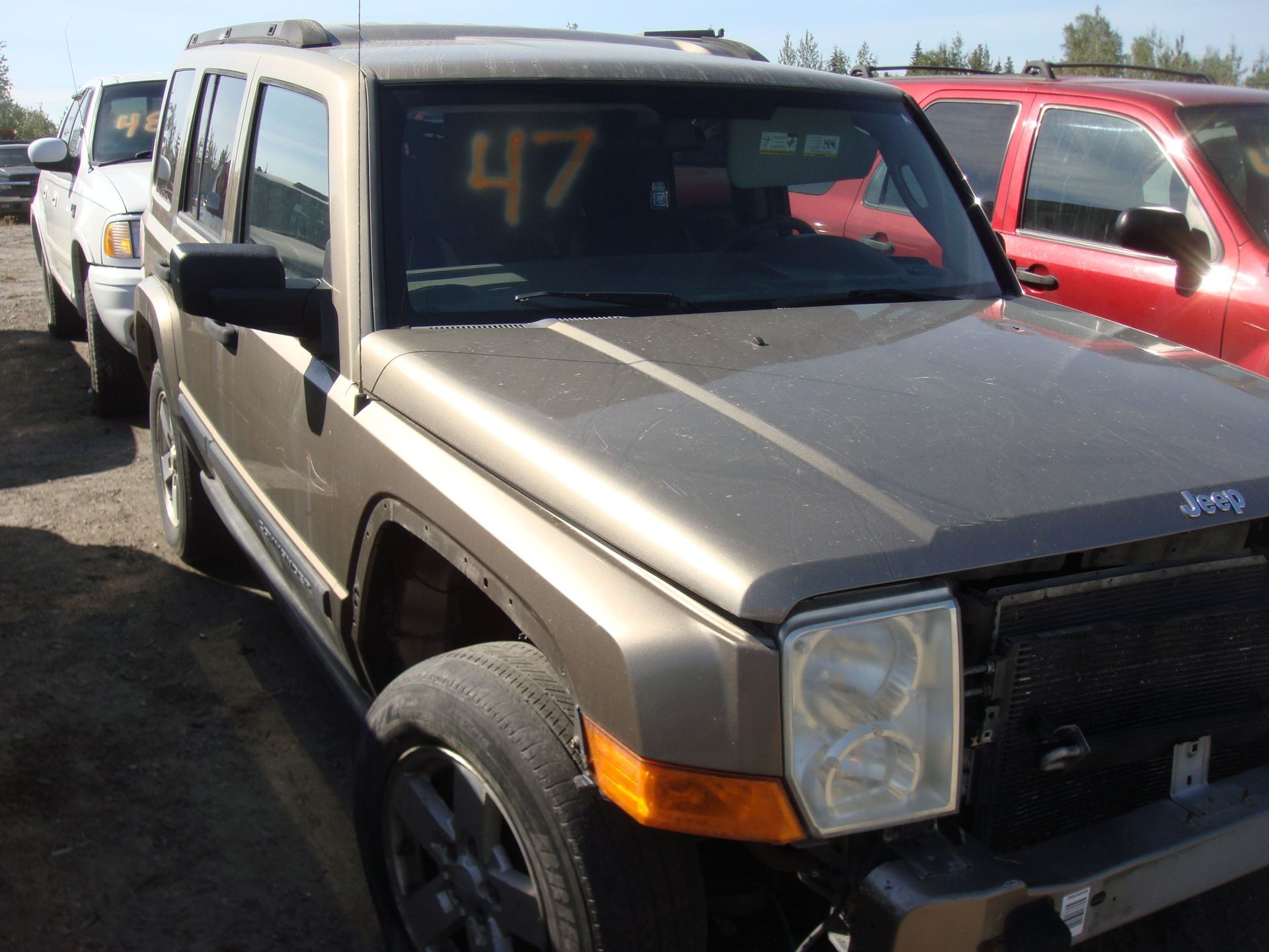 Dusty tan SUV parked outdoors beside a red vehicle, with yellow “47” written on the windshield.