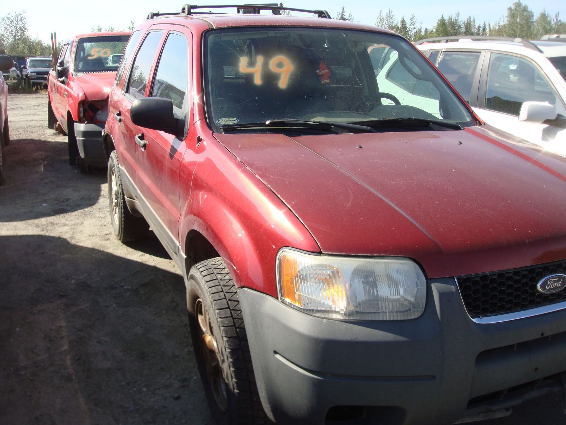 Red pickup truck in a car lot, with a yellow “49” on the windshield and another red truck behind it.