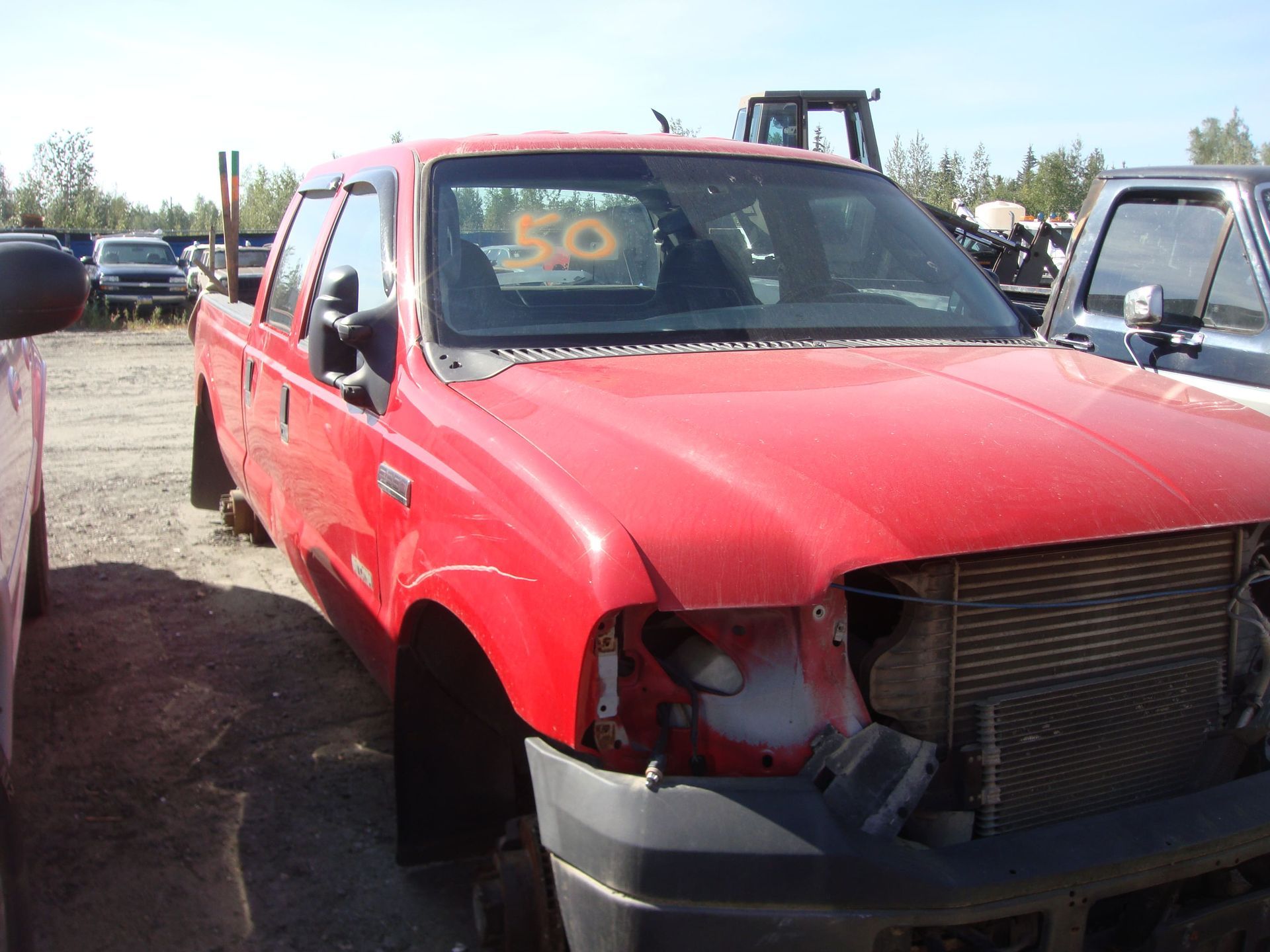 Red pickup truck with front-end damage parked in a lot, with a yellow “50” sign in the windshield.
