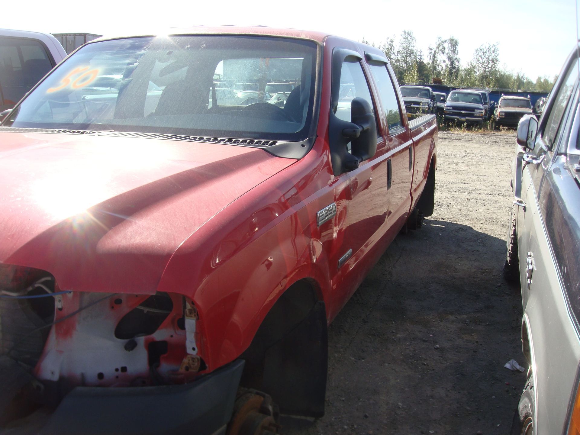 Damaged red pickup truck in a salvage yard, front bumper and headlight missing