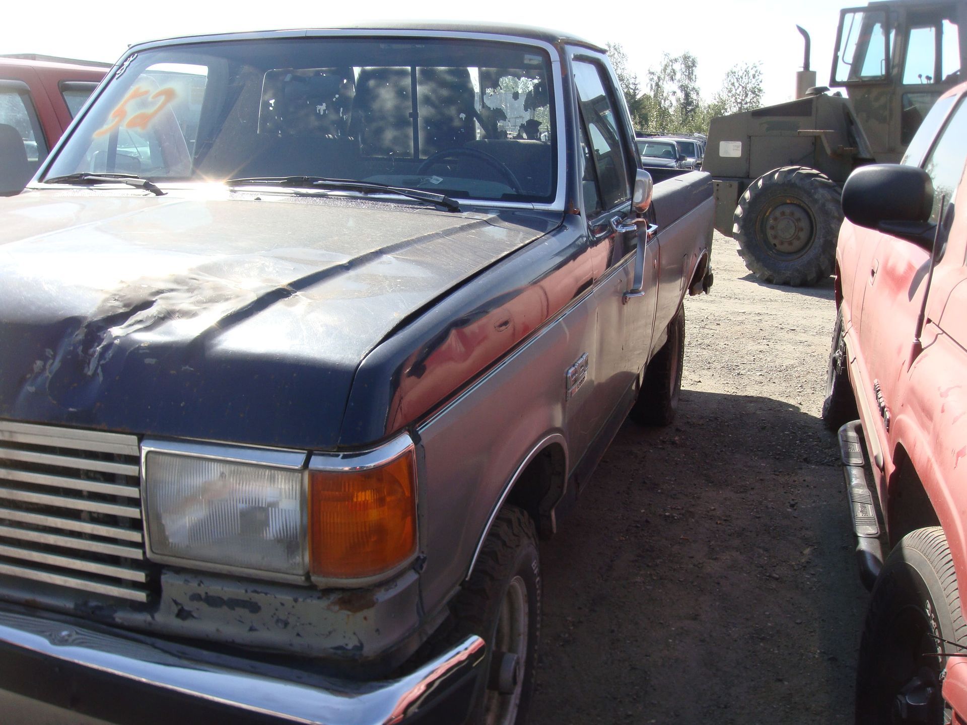 Old blue and red pickup trucks parked in a gravel lot, with a tractor in the background