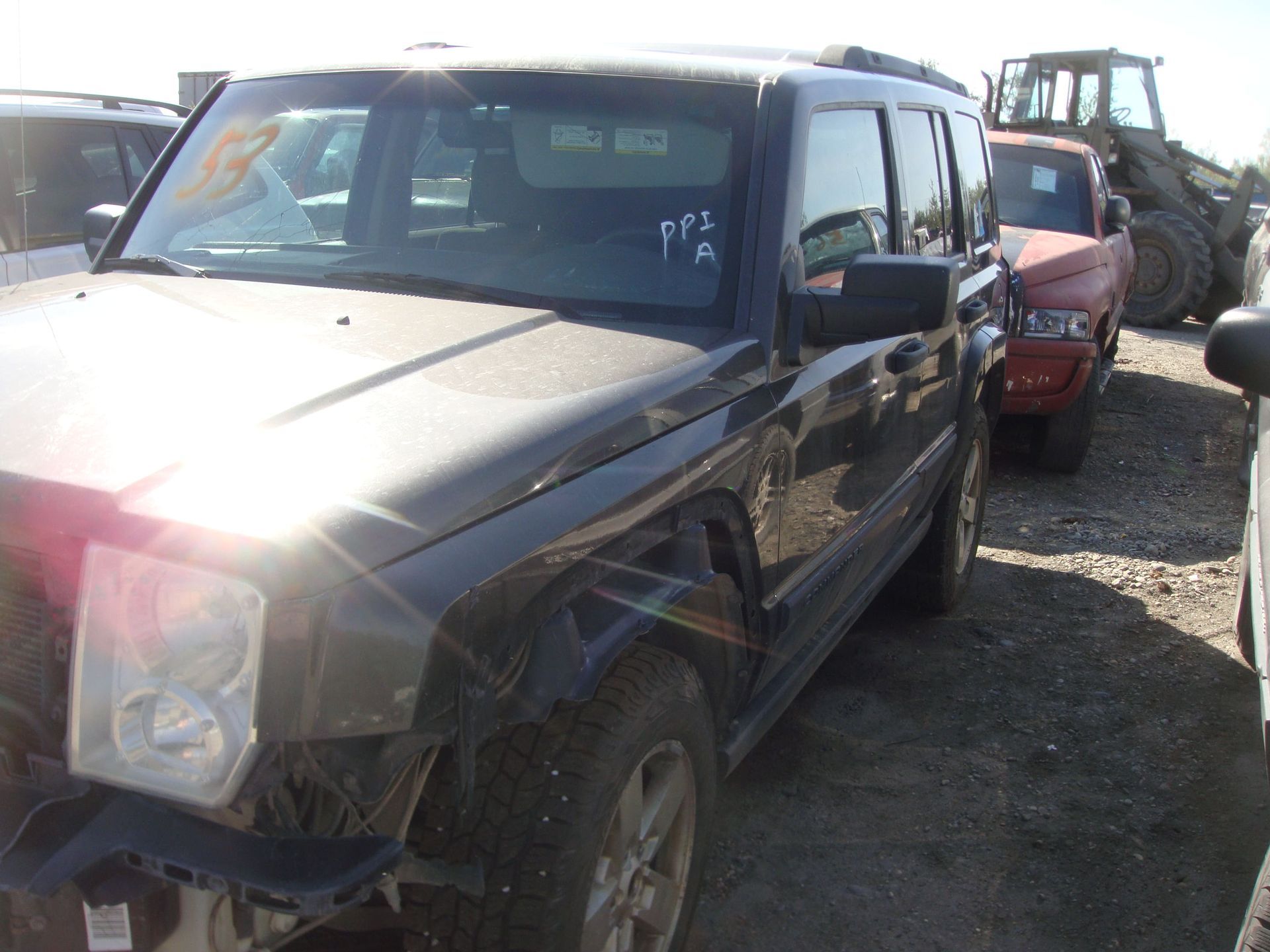 Damaged black SUV parked in a gravel lot, with another vehicle and equipment behind it