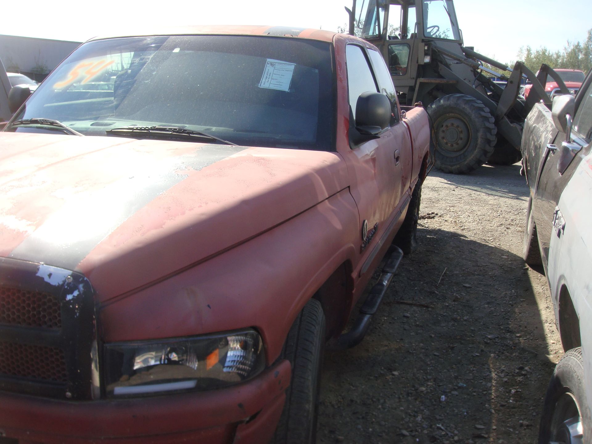 Red pickup truck parked in a gravel lot beside a large front loader.